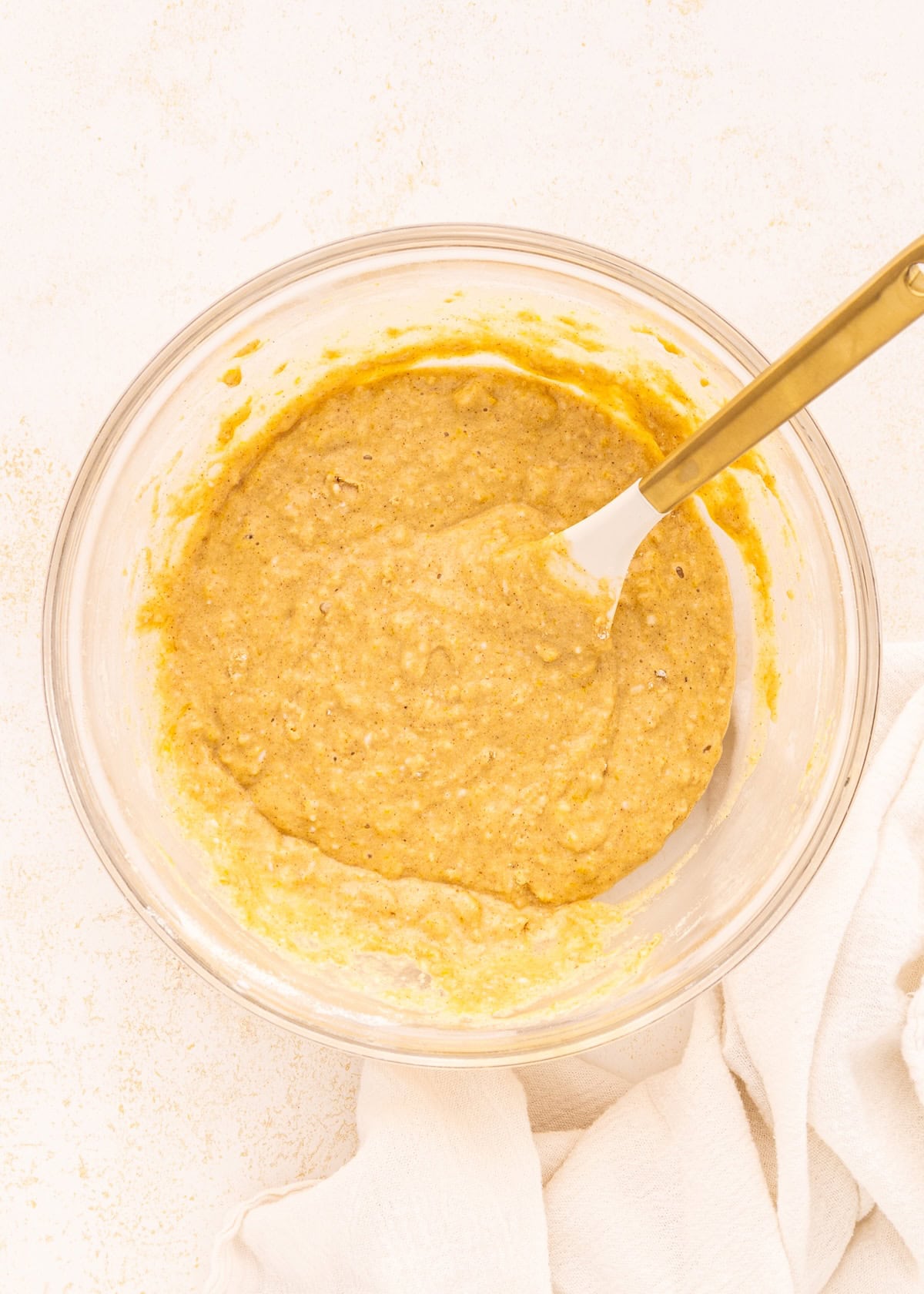 Bowl of thick batter with a spatula on a light surface, next to a white cloth.