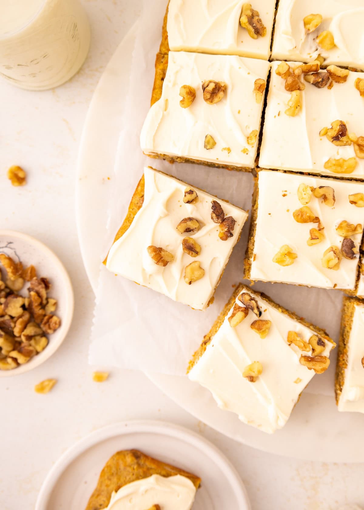 Frosted cake squares topped with walnuts on a white plate, with extra walnuts on the side.