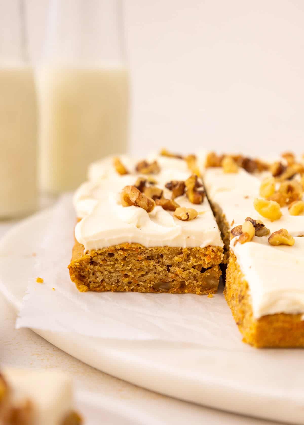 Frosted carrot cake bars topped with walnuts, with two glasses of milk in the background.