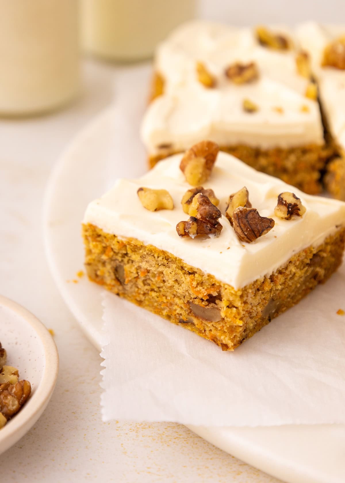 A carrot cake bar with cream cheese frosting and chopped walnuts on top.