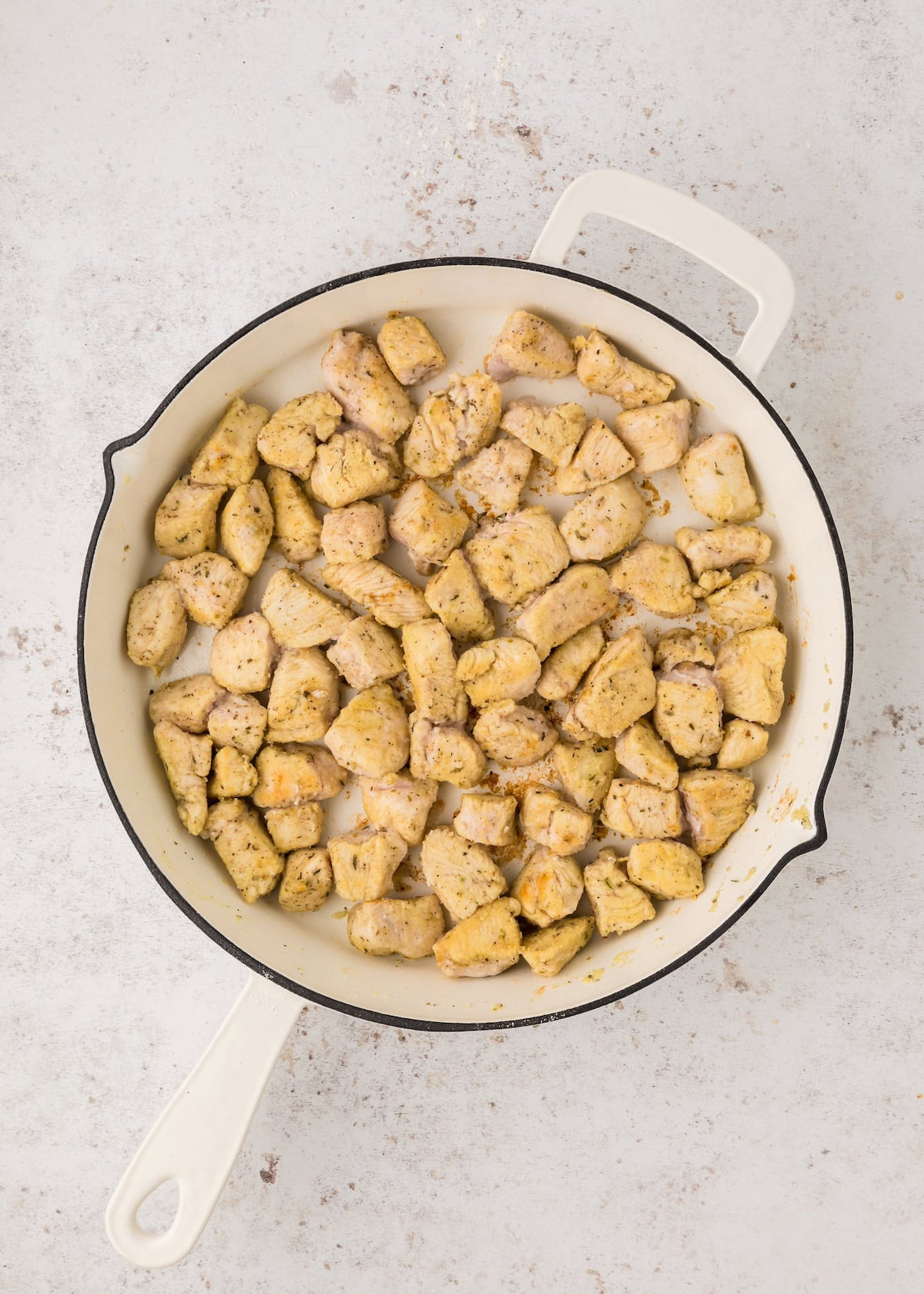 Cooked, seasoned chicken pieces in a white skillet on a light countertop.