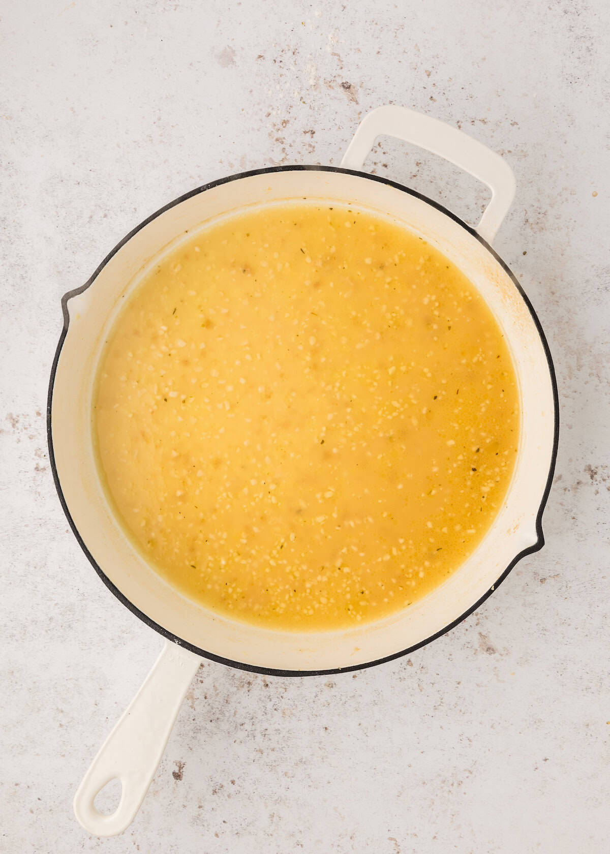 A white pot filled with yellow, creamy soup on a light-colored surface.