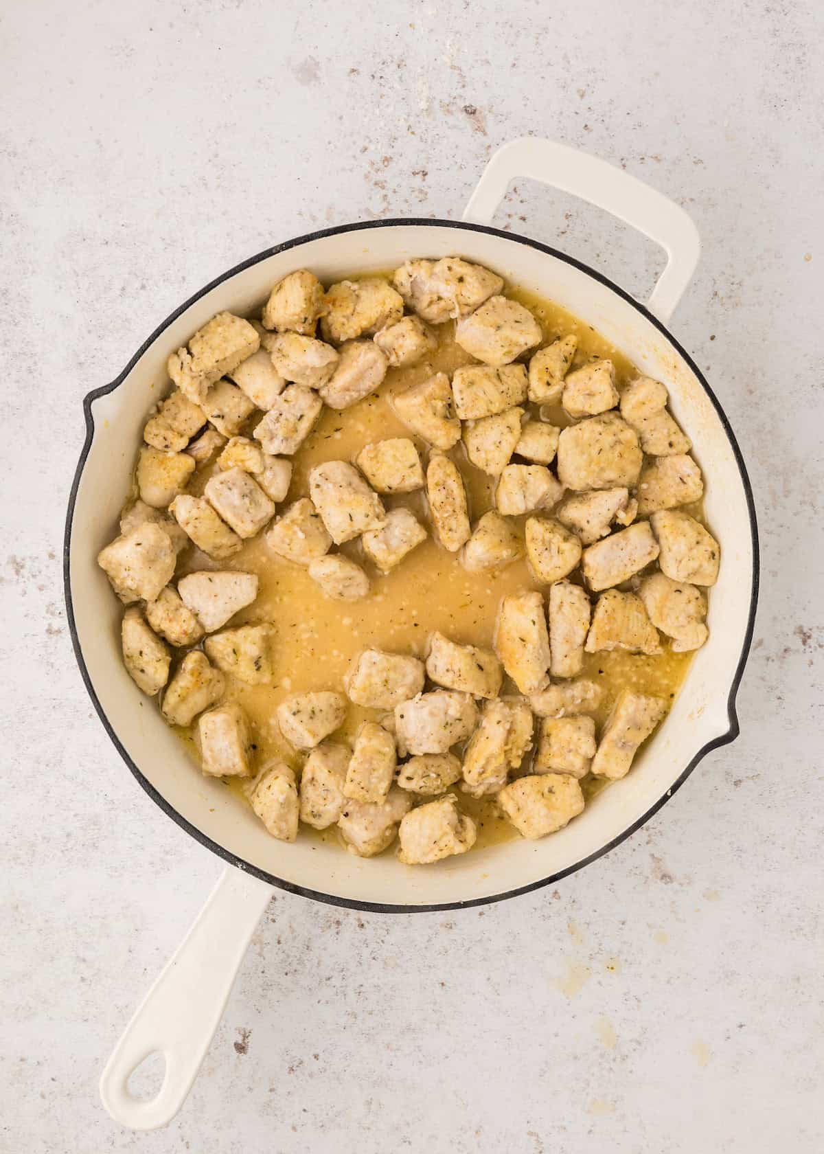 Chunks of seasoned tofu cooking in a white skillet with a light sauce.