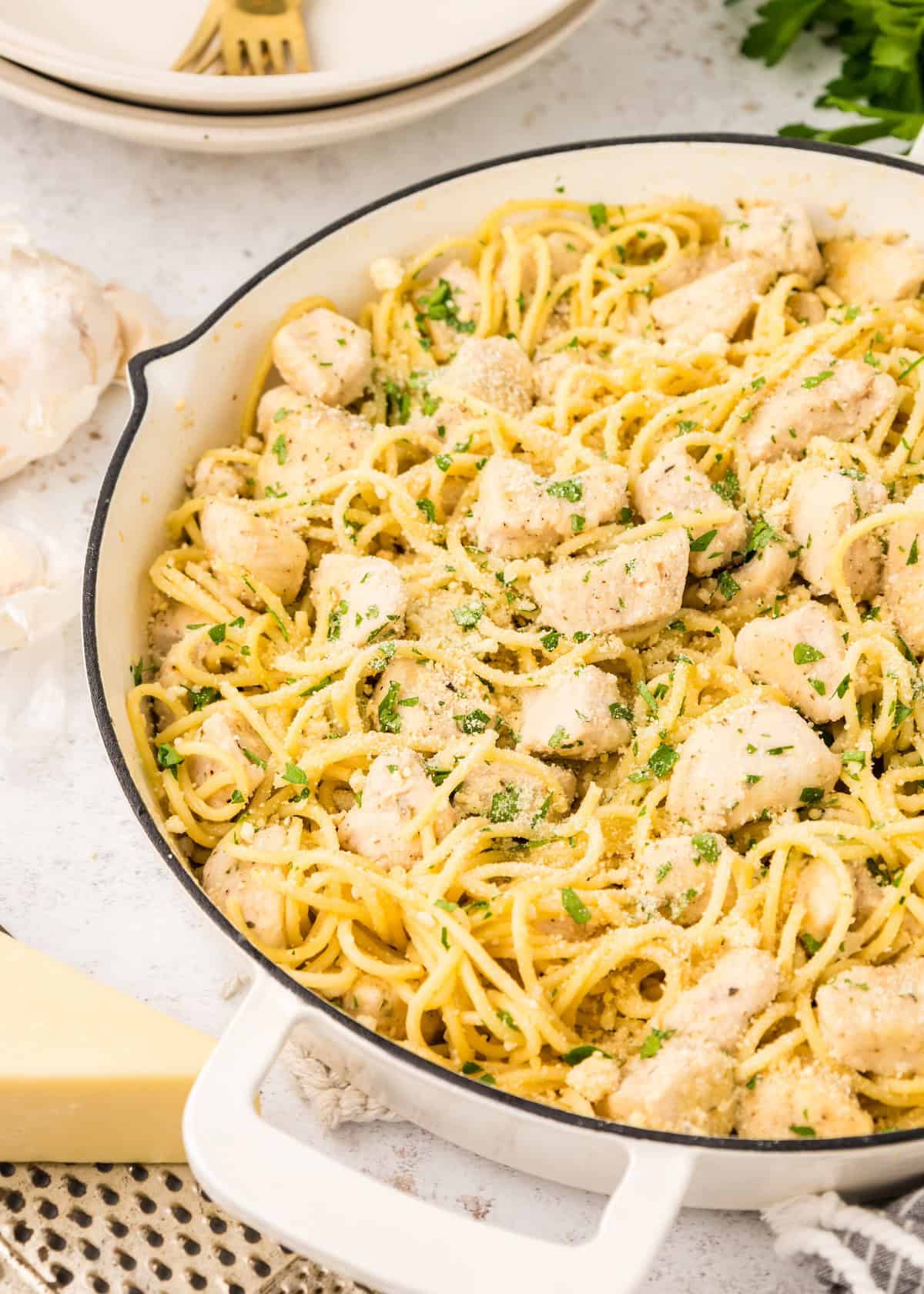 A pan of creamy chicken spaghetti garnished with chopped parsley and grated cheese.