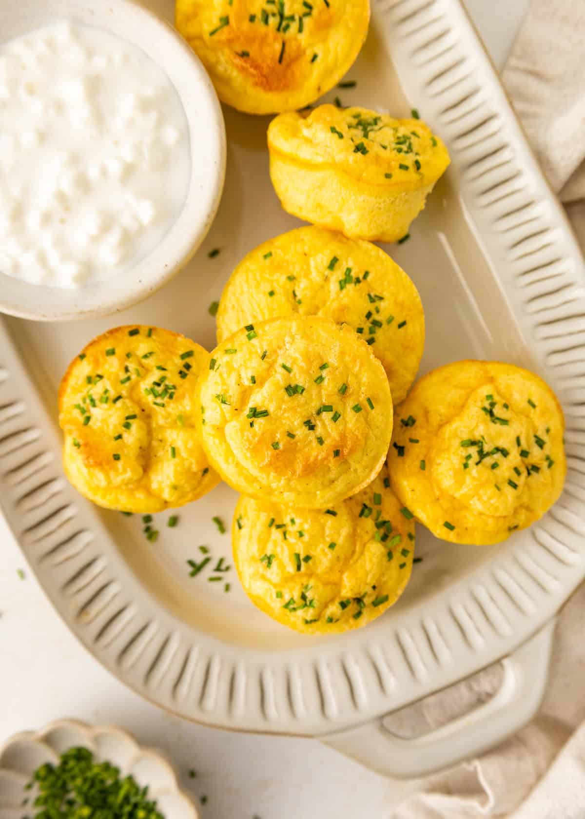 Mini egg muffins topped with chives on a white tray, with a bowl of cottage cheese.
