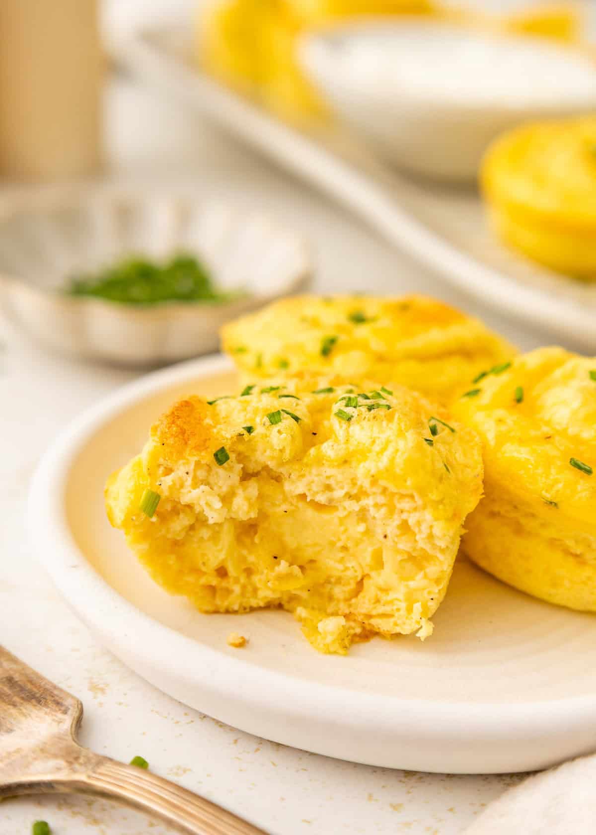 Egg bites topped with chopped chives on a plate, one with a bite taken out.