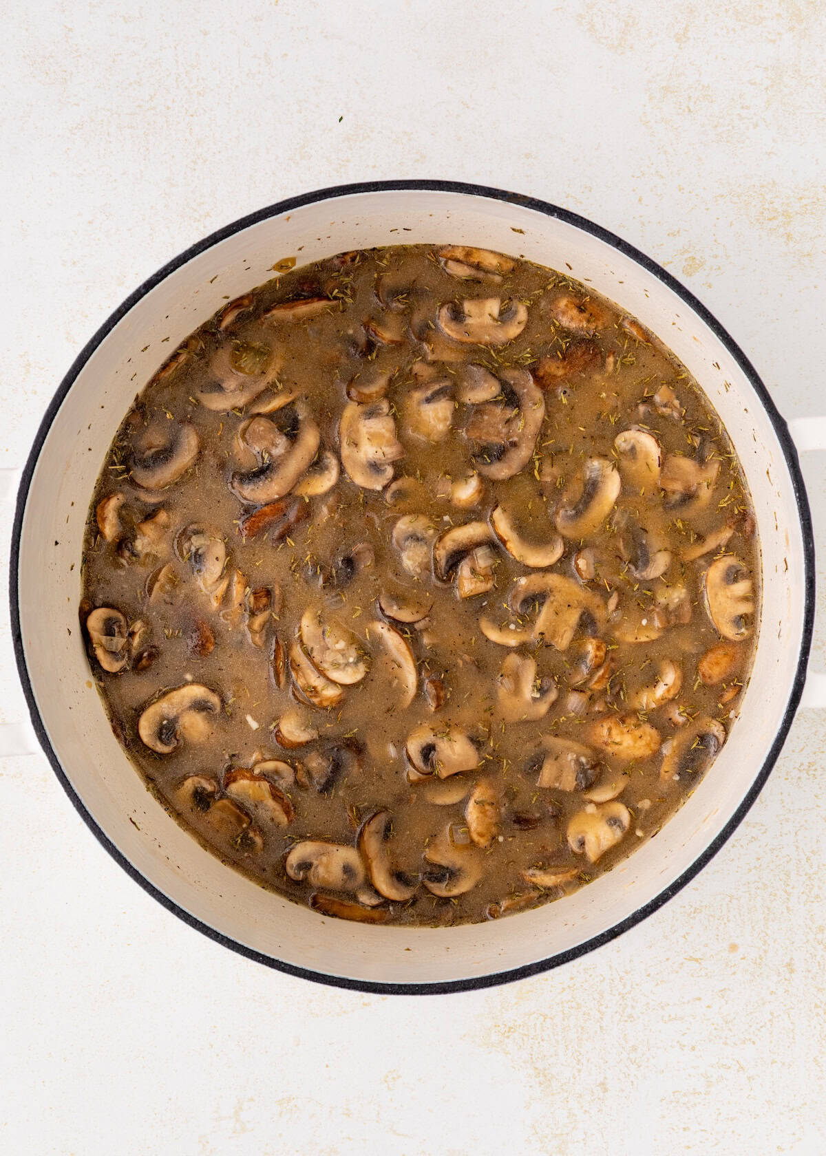 A pot filled with sliced mushrooms cooking in a brown broth.