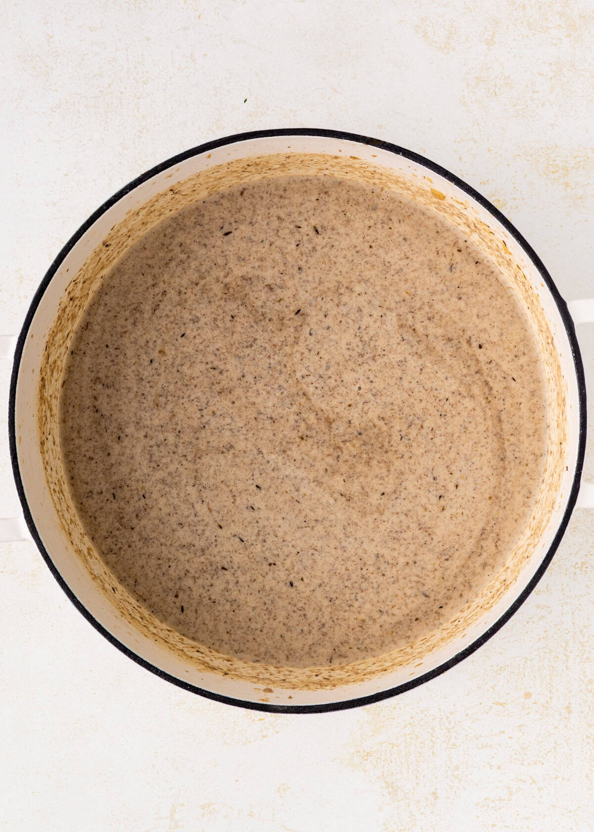 A pot filled with creamy mushroom soup on a white surface.