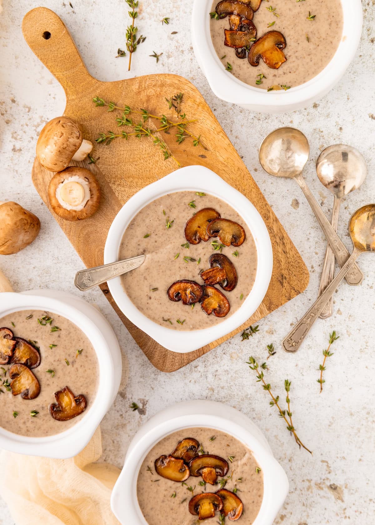 Four bowls of creamy mushroom soup, garnished with sautéed mushrooms and fresh herbs.
