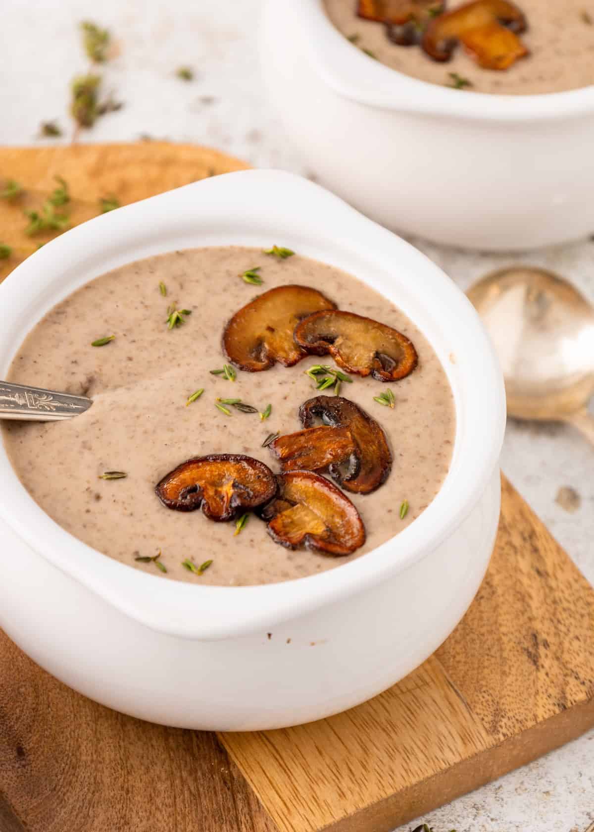 Creamy mushroom soup in a white bowl, topped with sautéed mushrooms and herbs.