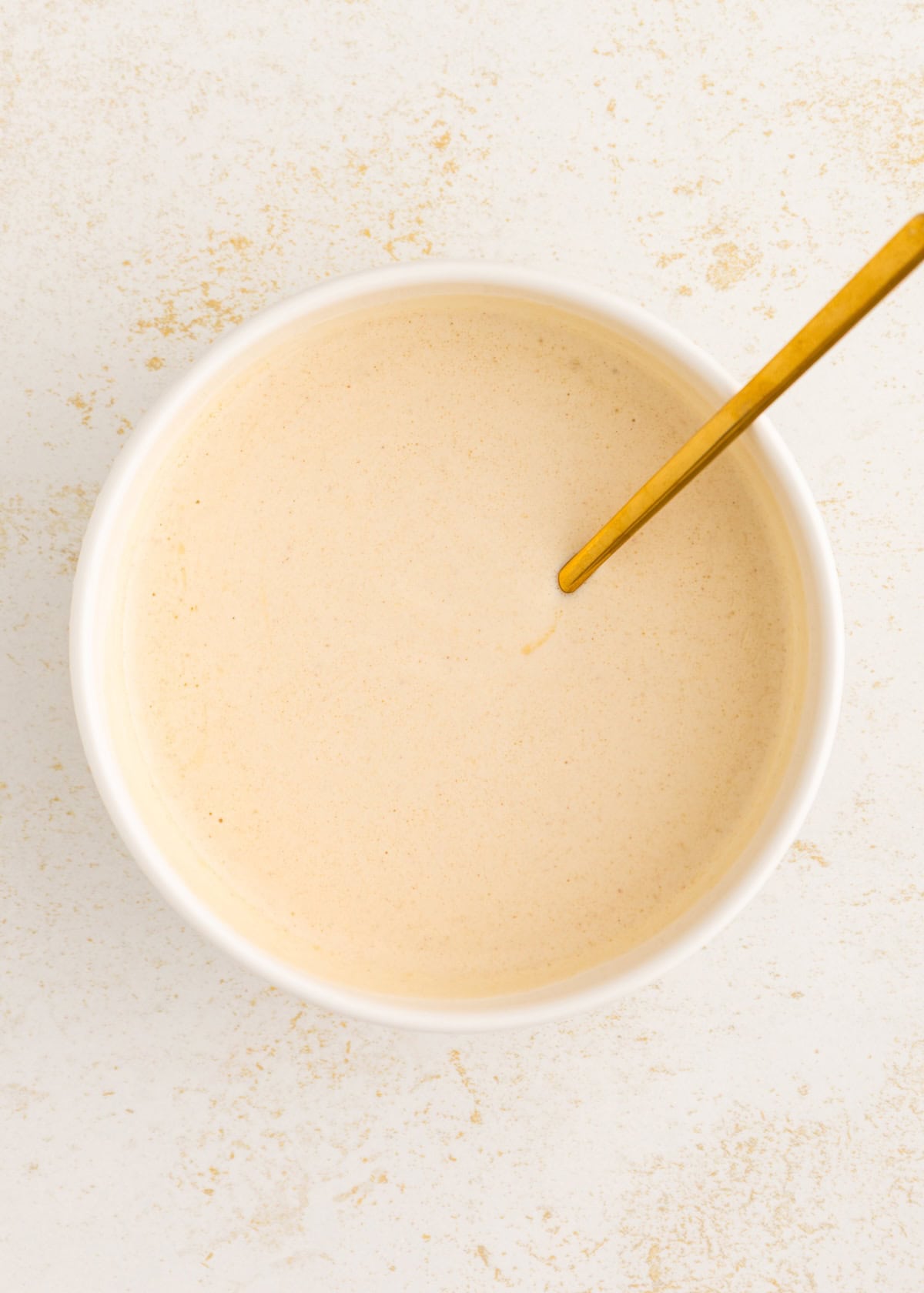 A white bowl of creamy Italian dressing with a gold spoon on a light surface.