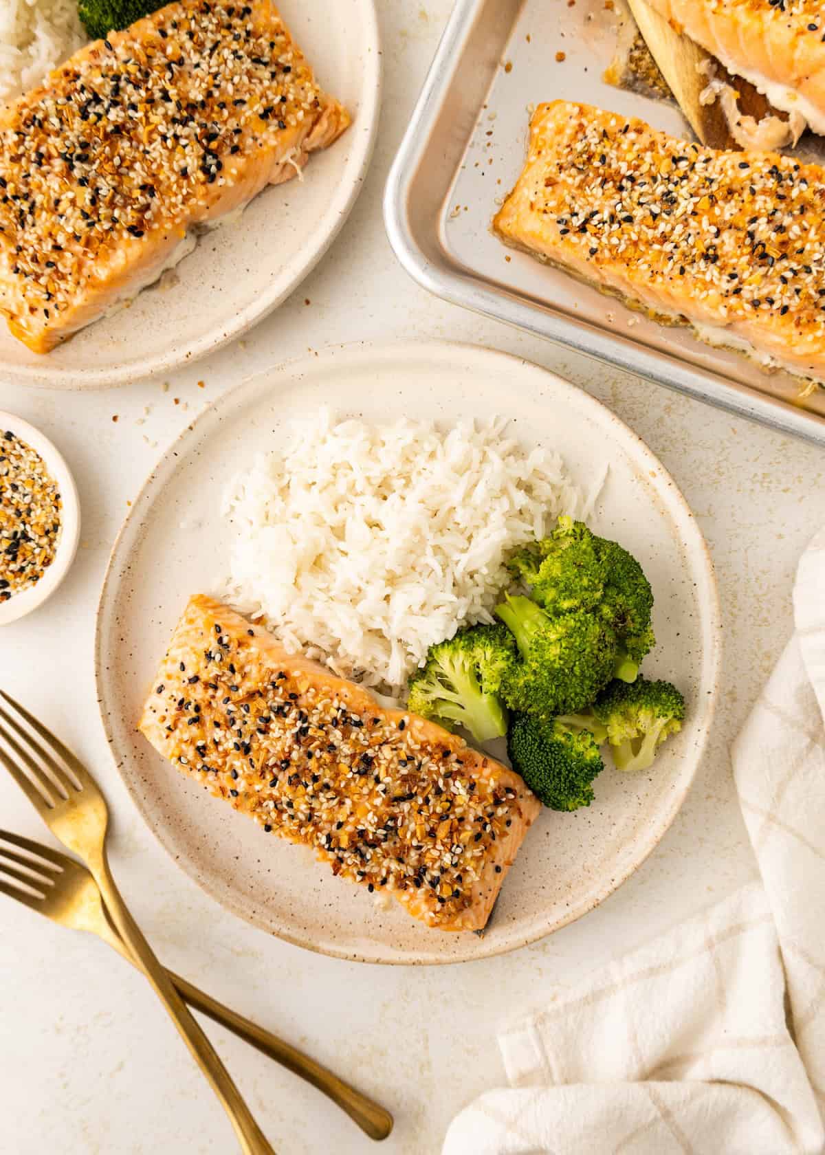Plate with sesame-crusted salmon, white rice, and broccoli on a light table setting.