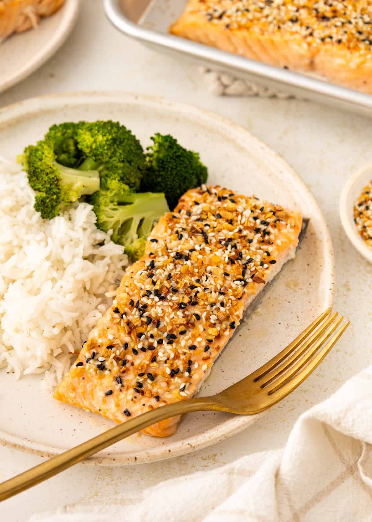 A plate with sesame-crusted salmon, white rice, and steamed broccoli, with a gold fork.
