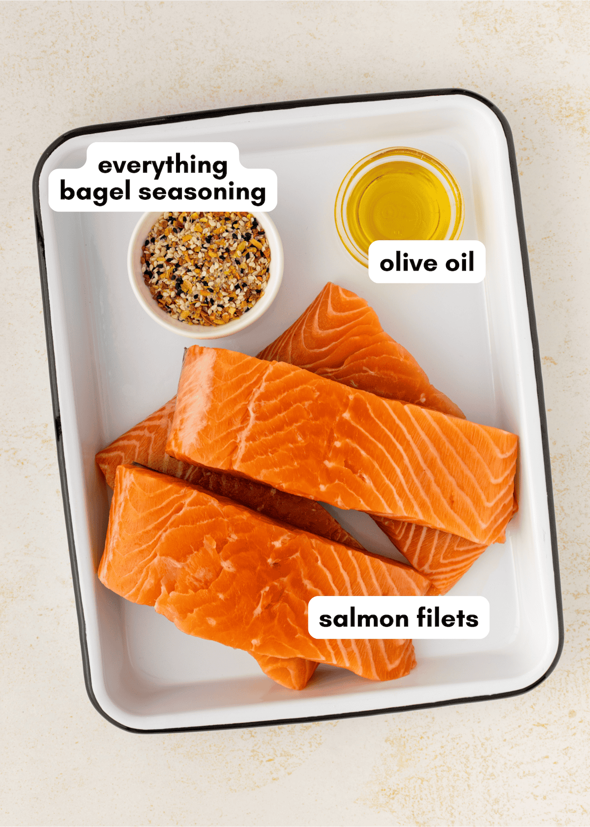 Three raw salmon filets, a small bowl of olive oil, and everything bagel seasoning in a tray.