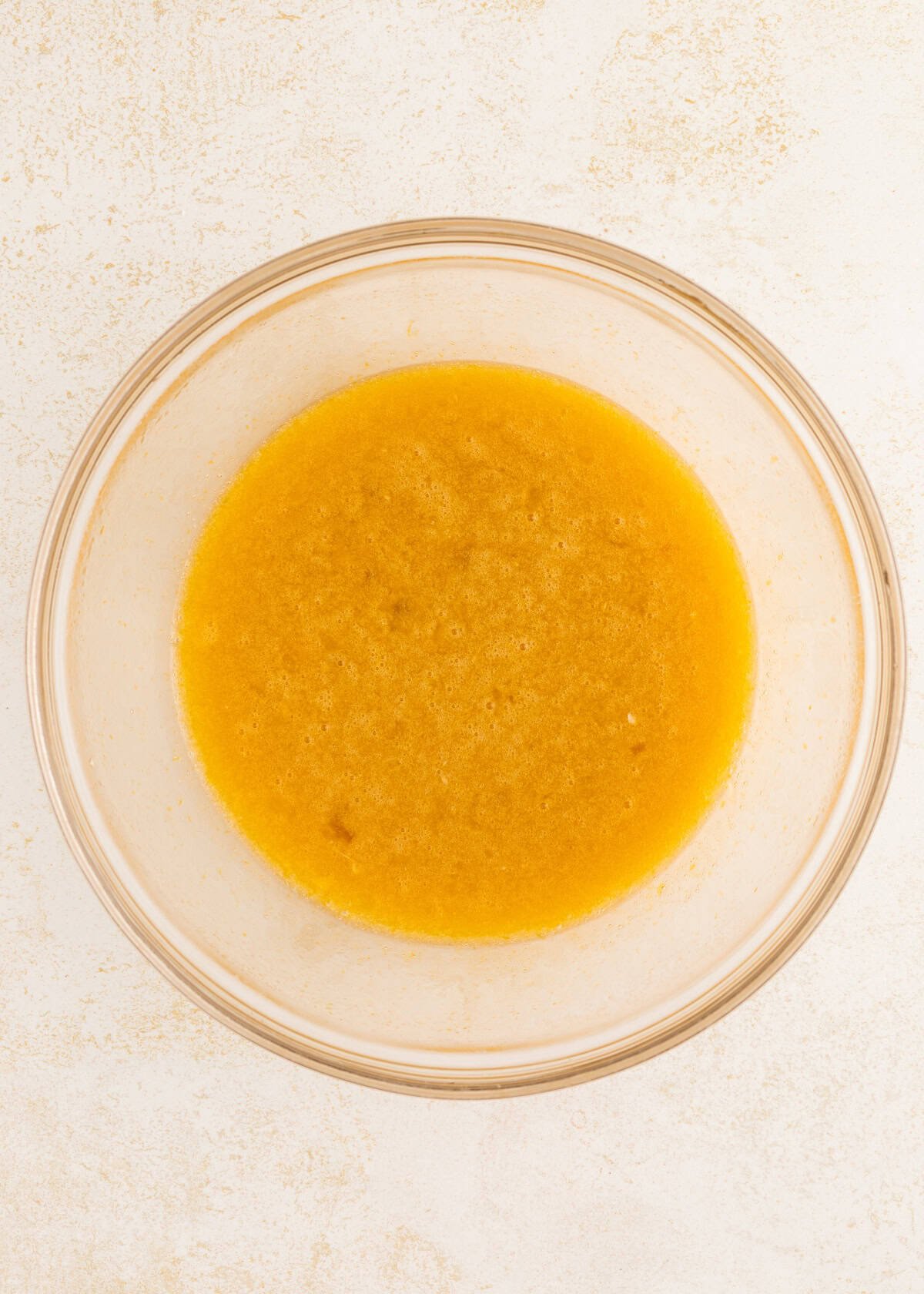 Glass bowl filled with yellowish liquid mixture on a light, textured surface.