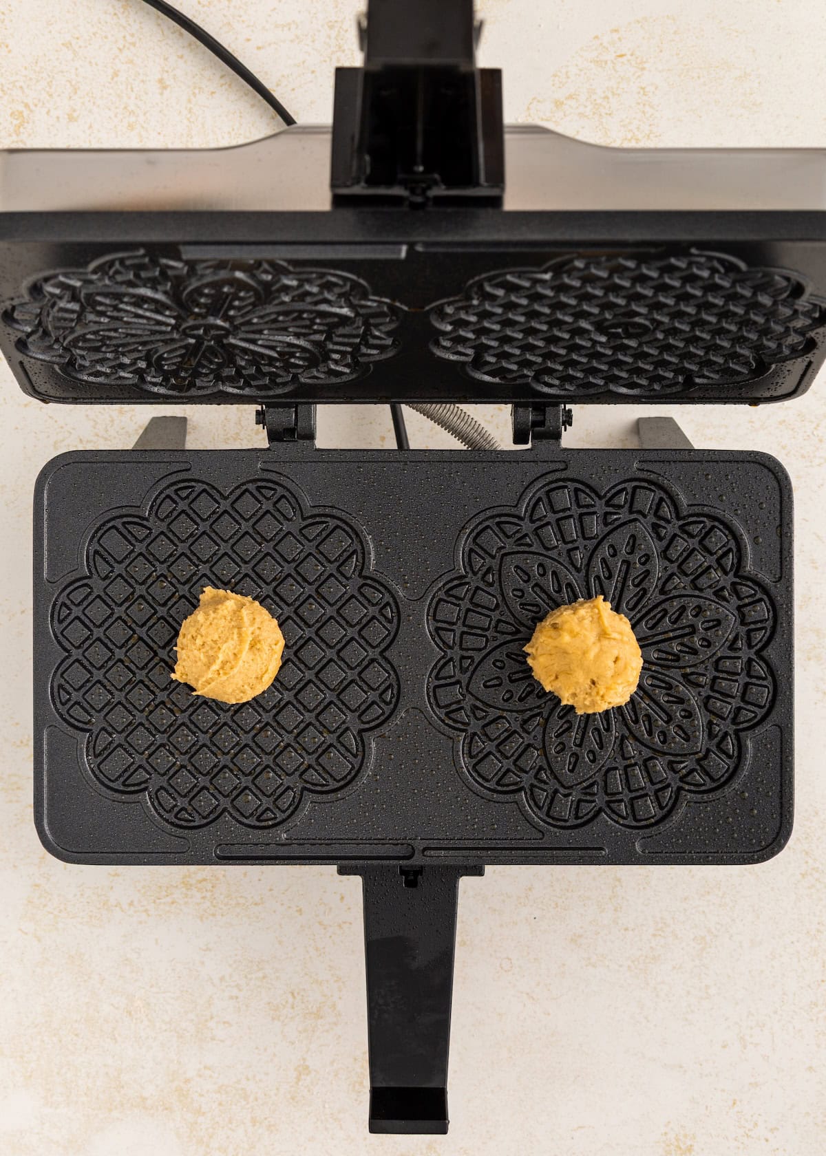 Two scoops of dough placed on a patterned pizzelle maker, ready to be cooked.