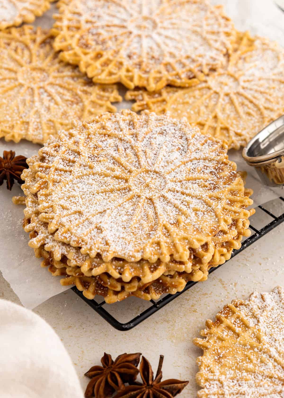 A stack of pizzelle cookies dusted with powdered sugar on a cooling rack.