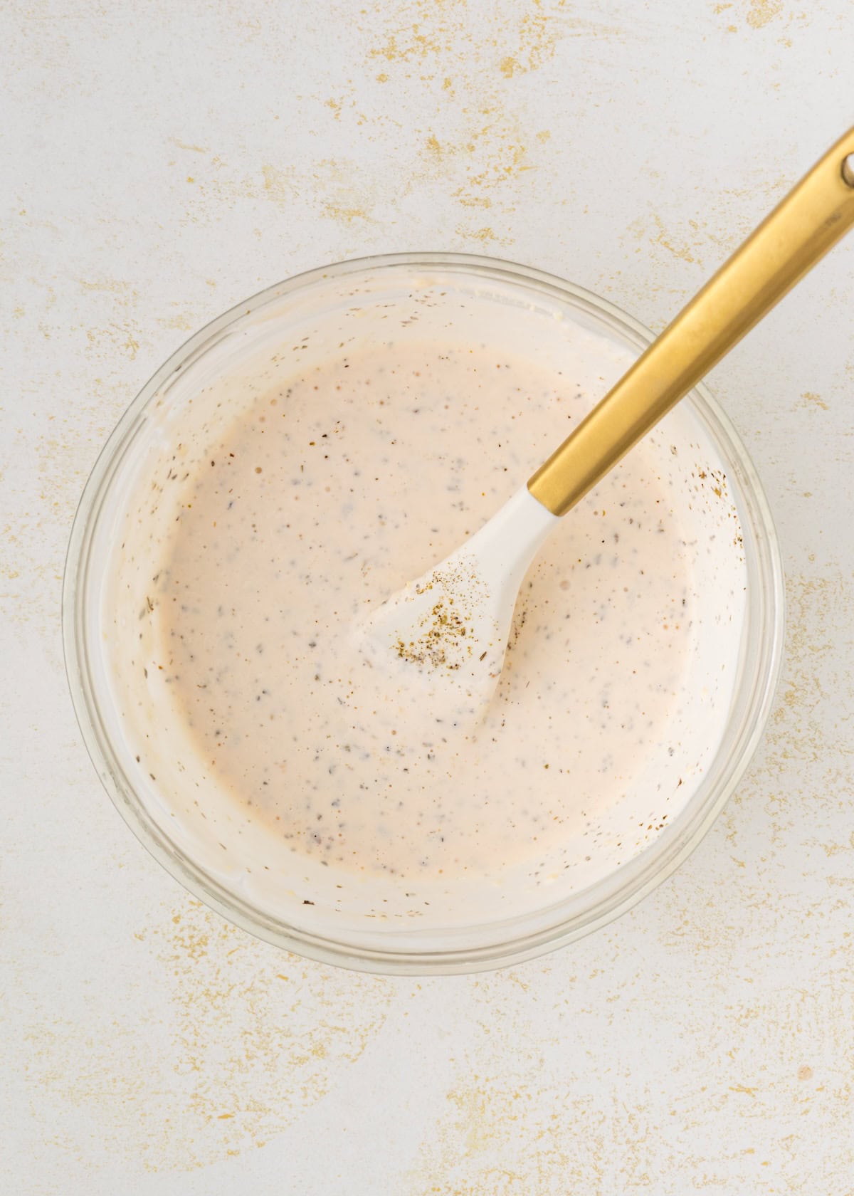 A bowl of creamy sauce with black specks, stirred with a white and gold spoon.