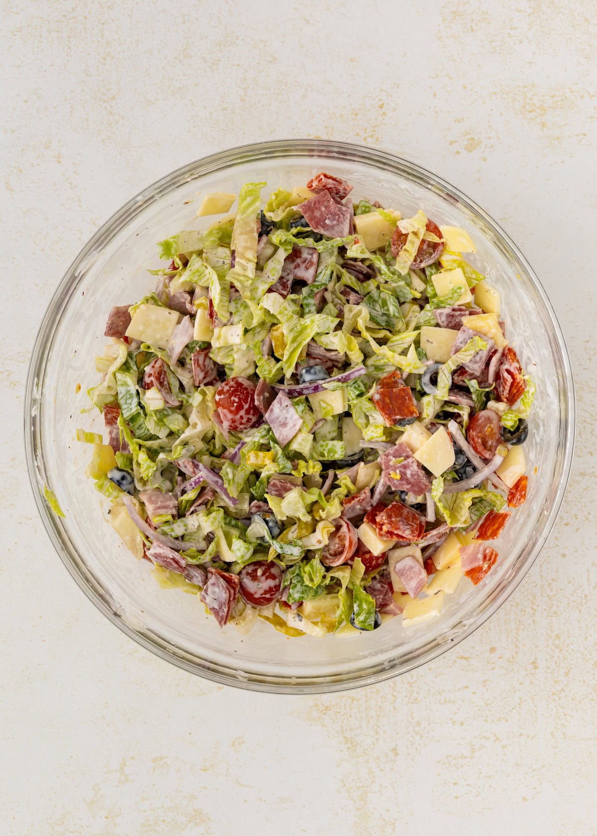 Glass bowl filled with chopped salad, deli meats, cheese, tomatoes, and lettuce.