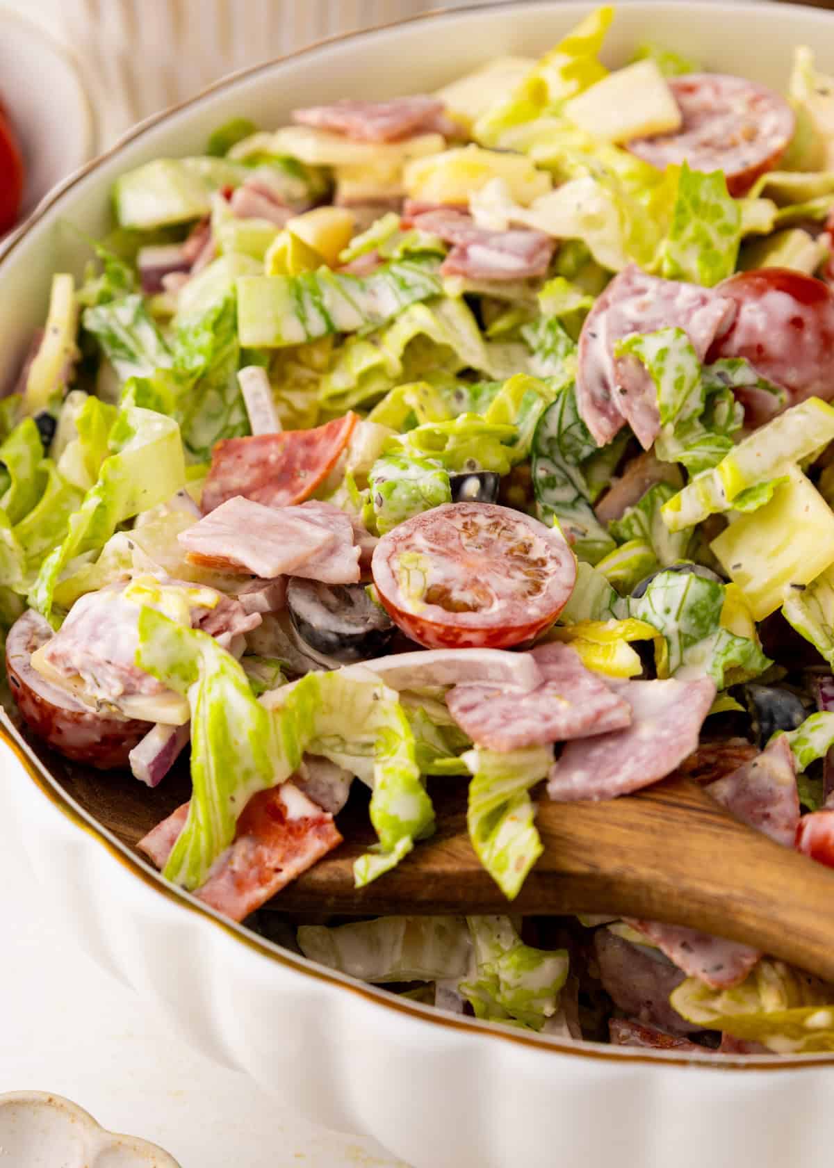 A close-up of a creamy salad with lettuce, tomatoes, olives, and sliced deli meats in a bowl.