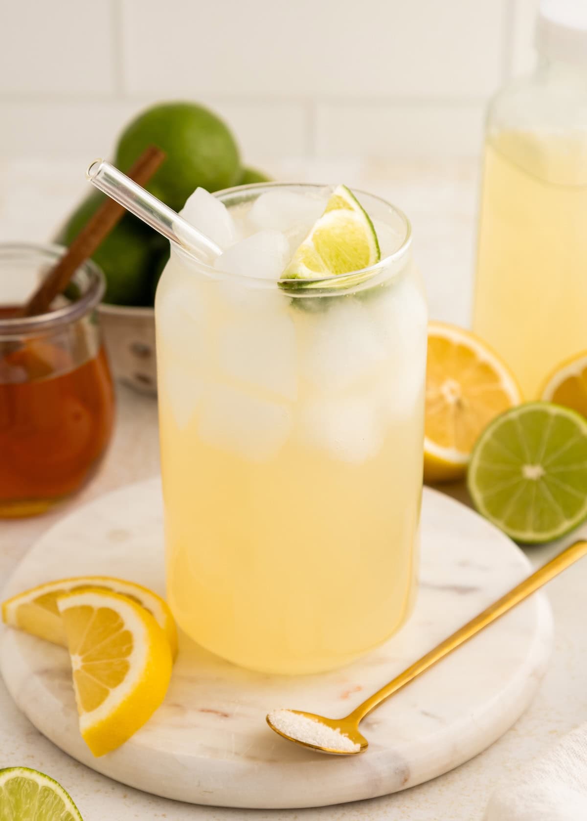Iced lemon-lime drink in a glass with a straw, surrounded by citrus slices and honey jar.