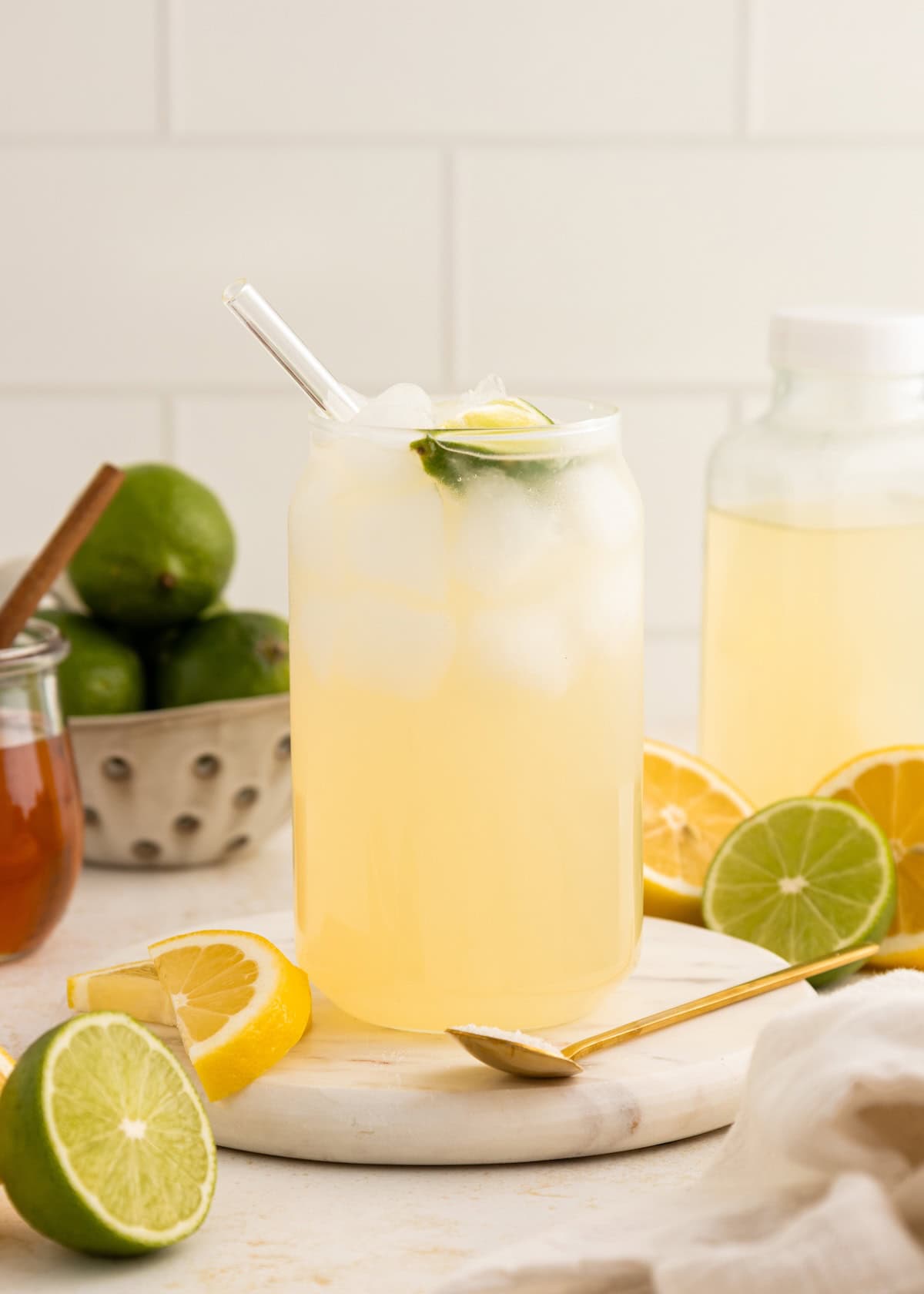 Iced lemonade in a glass with a straw, surrounded by fresh lemons and limes.