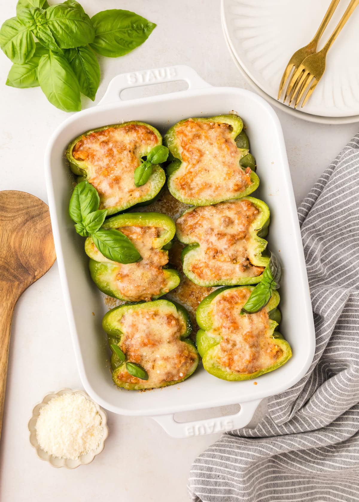 Stuffed green bell peppers with melted cheese in a white baking dish, garnished with basil.