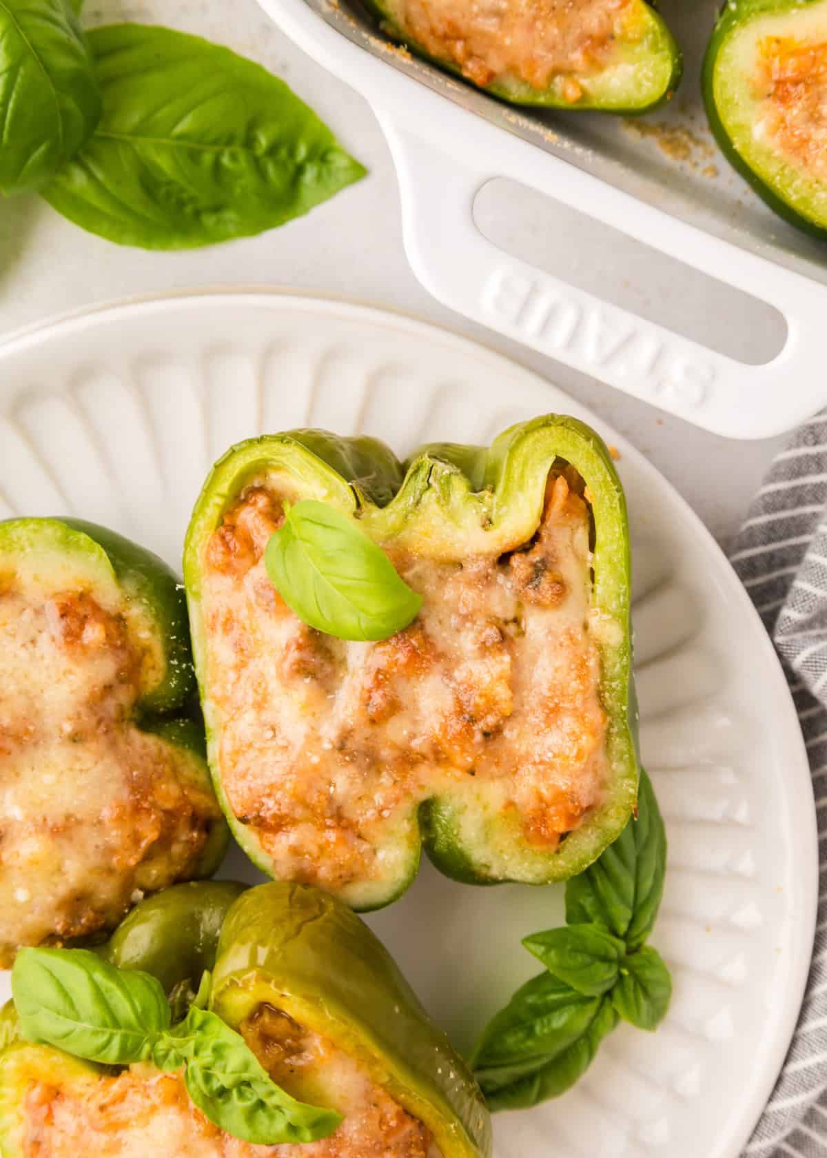Green bell peppers stuffed with meat and cheese, garnished with fresh basil on a white plate.