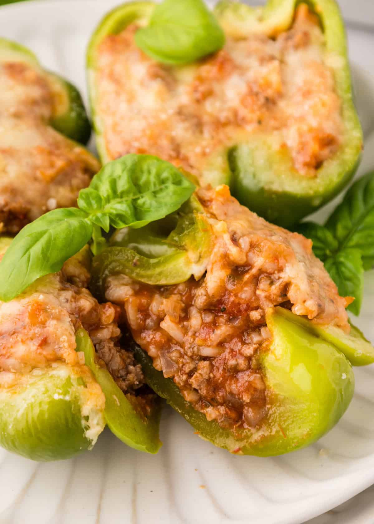 Stuffed green bell peppers with ground meat, tomato sauce, cheese, and fresh basil on a plate.