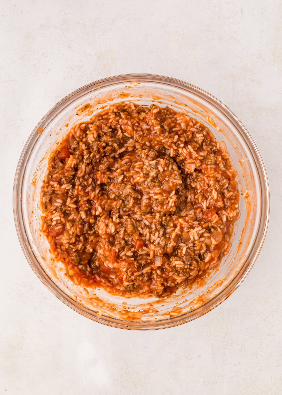 A glass bowl filled with a mixture of rice, ground meat, and tomato sauce.
