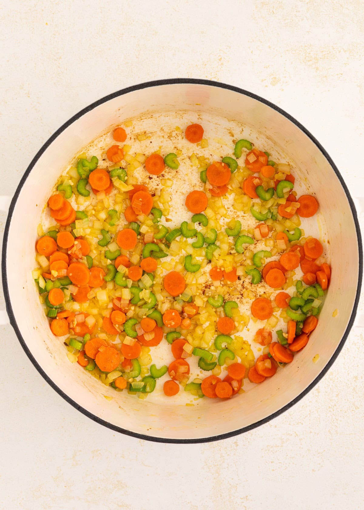 Chopped carrots, celery, and onions sautéing for delicious Italian Wedding Soup in a white pot.