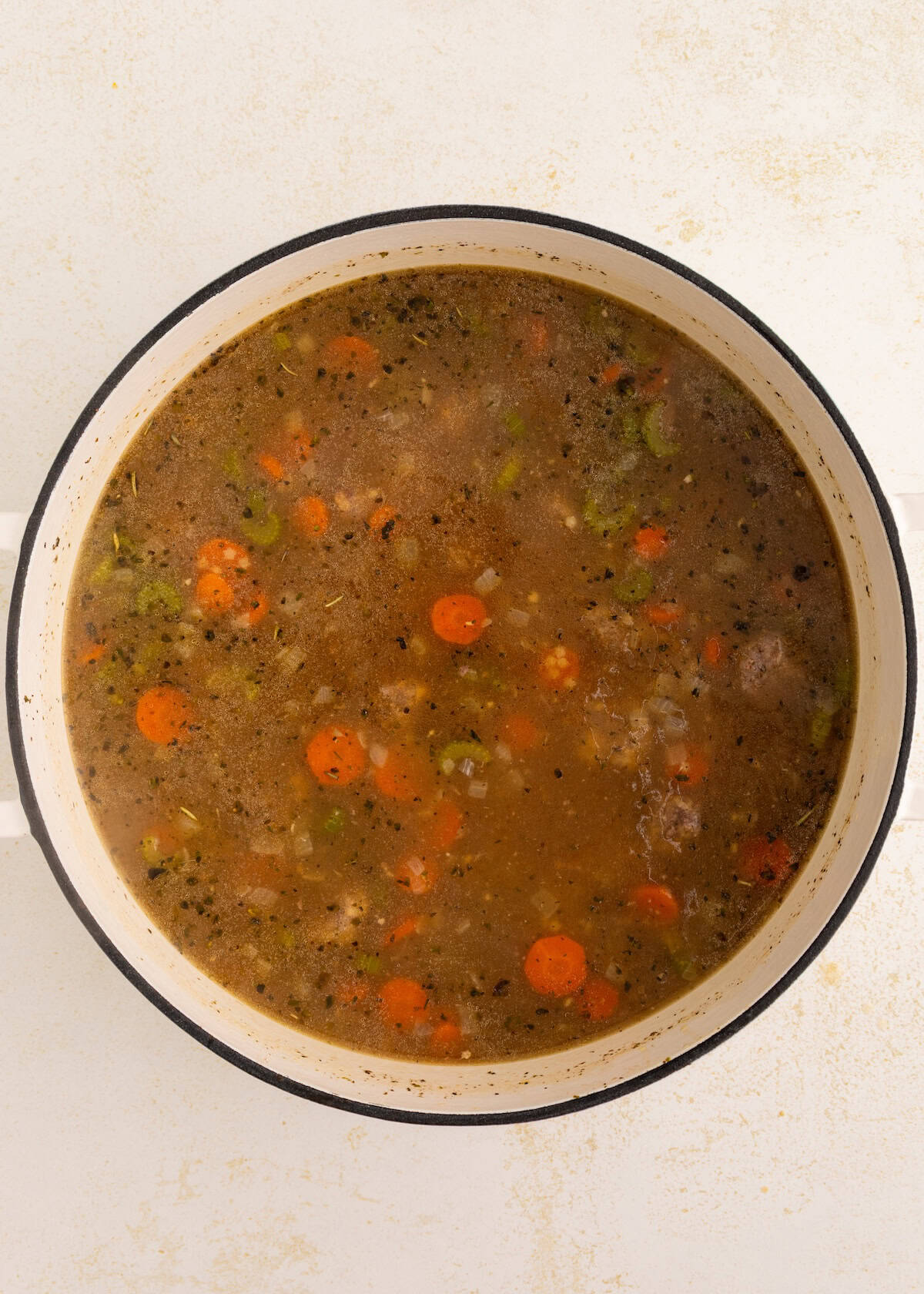 A pot of Italian Wedding Soup with carrots, celery, and herbs simmering on a stovetop.