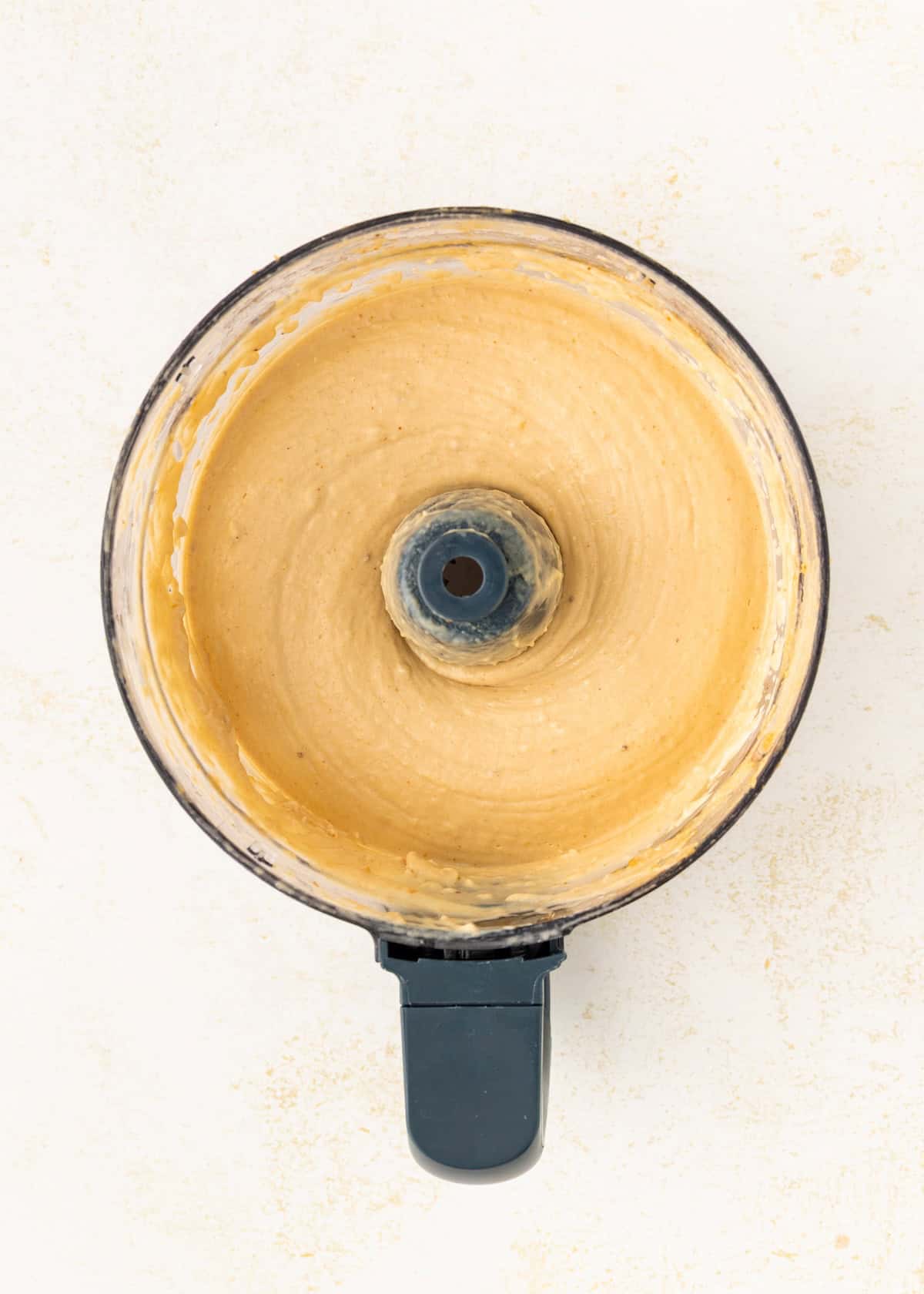 Top view of creamy, blended mixture in a food processor on a light background.