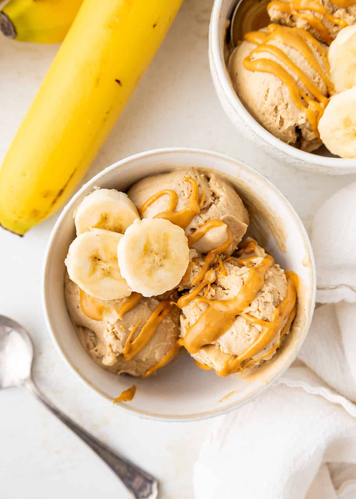 Bowl of ice cream topped with banana slices and peanut butter, next to a whole banana.