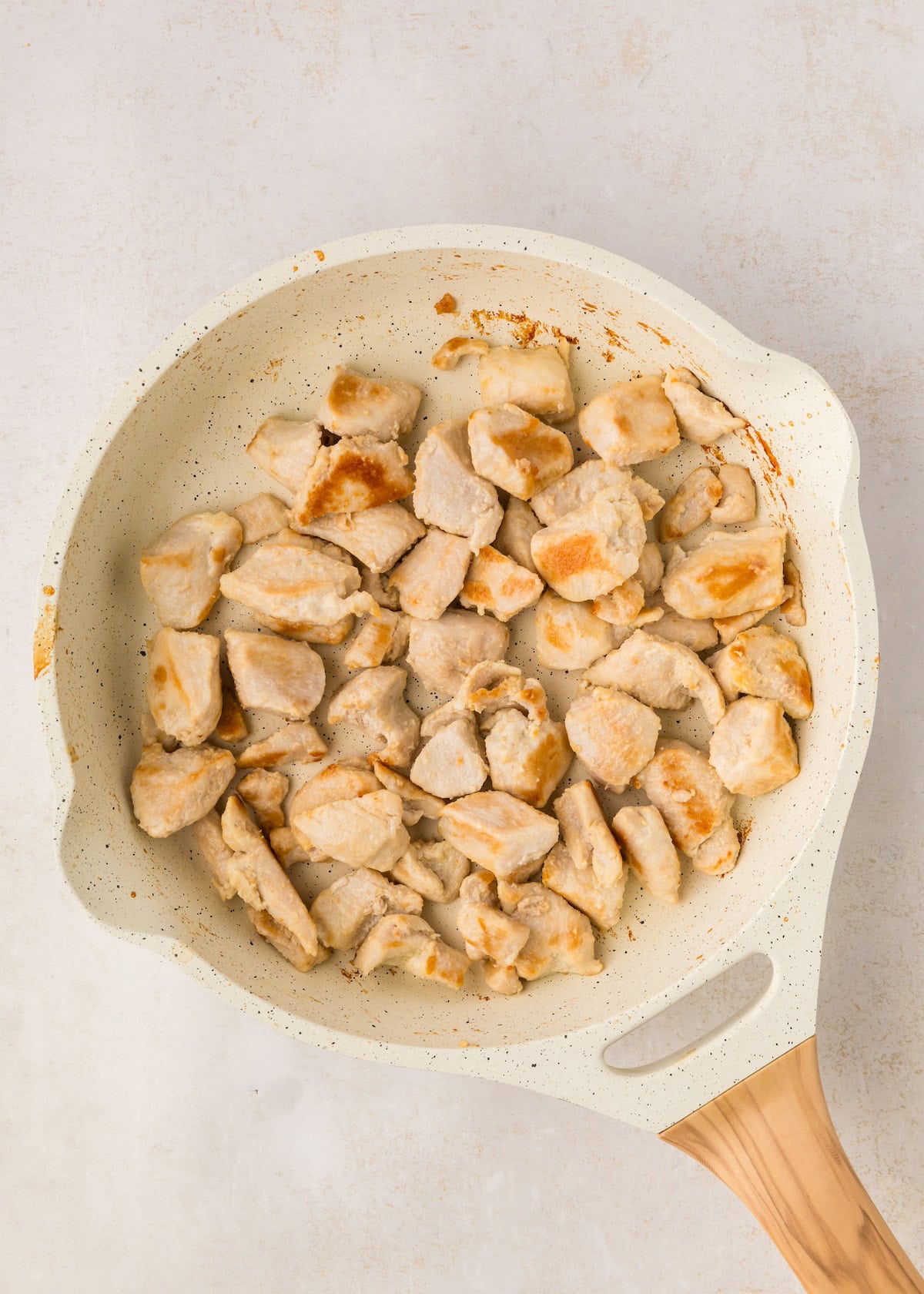 Cooked pieces of chicken breast in a white frying pan with a wooden handle.