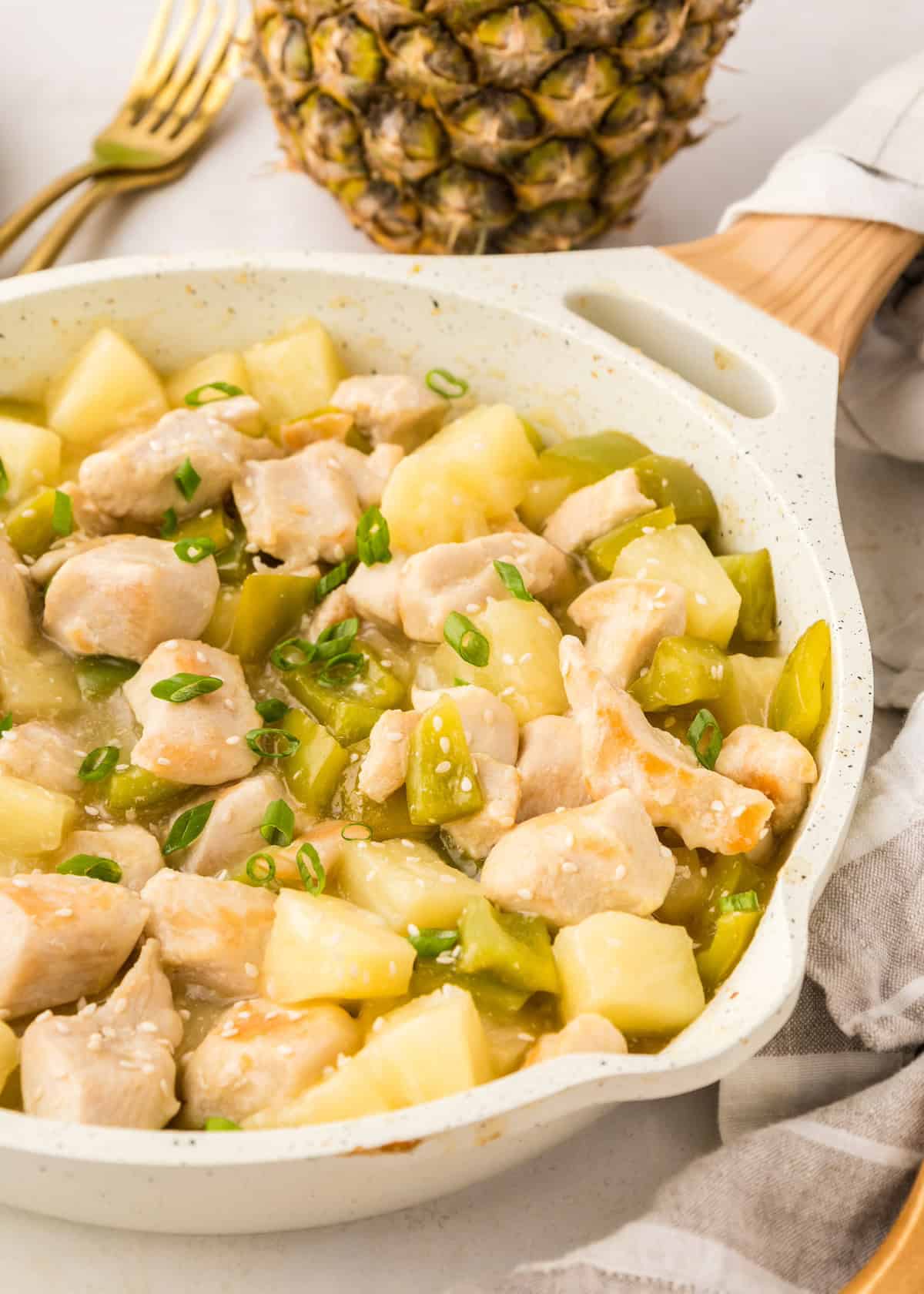 Chicken and pineapple stir-fry with green peppers in a white skillet, topped with green onions.