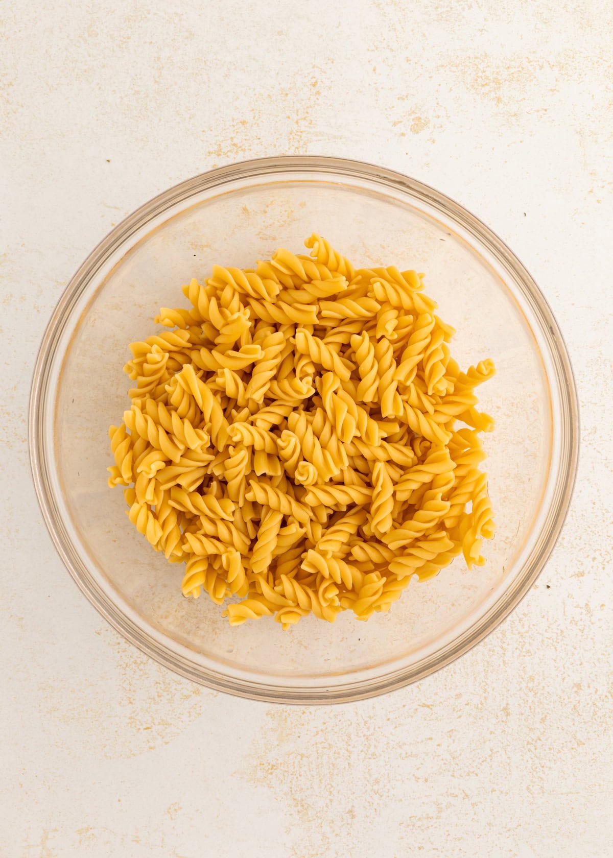 A glass bowl filled with dry rotini, perfect for making a protein pasta salad.