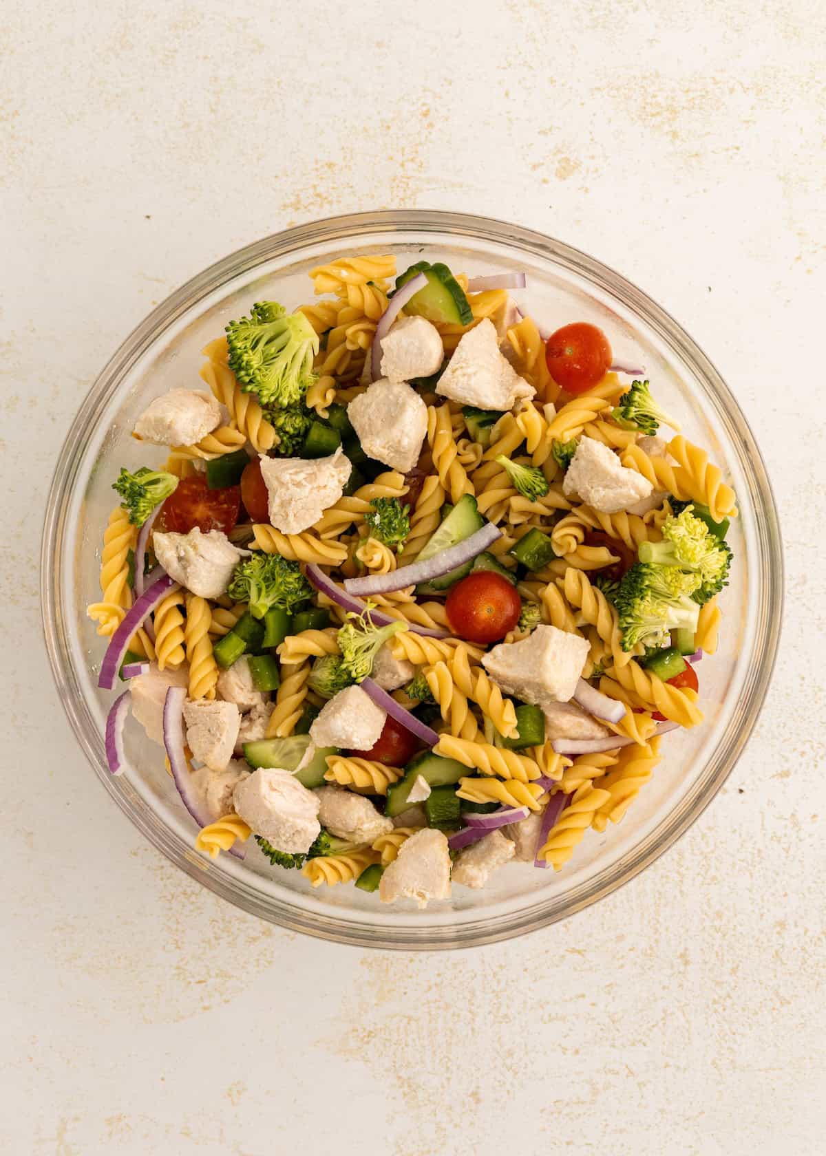 Protein pasta salad with chicken, broccoli, tomatoes, cucumber, and red onion in a glass bowl.