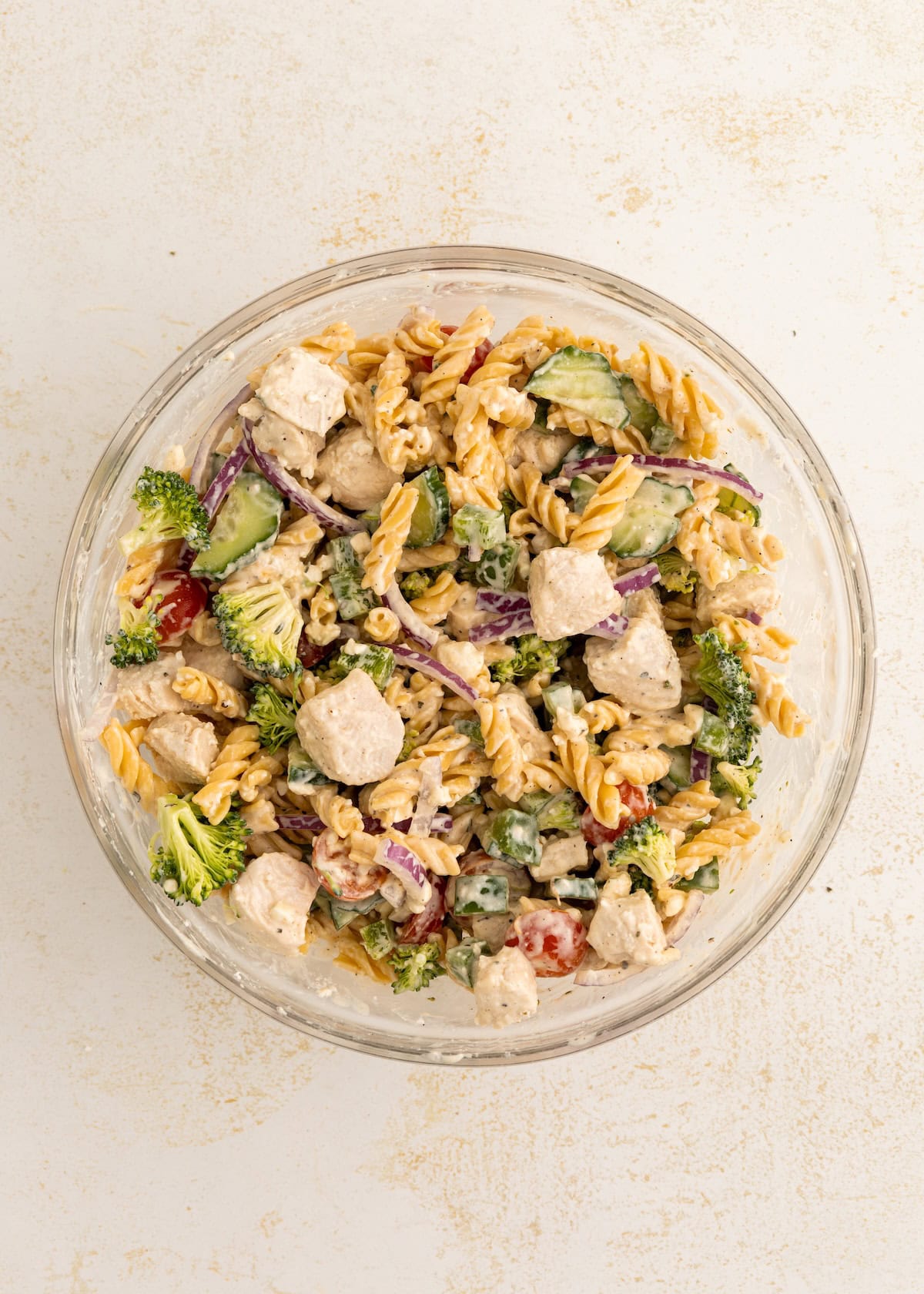 A bowl of protein pasta salad with chicken, broccoli, cucumber, tomatoes, and red onion.