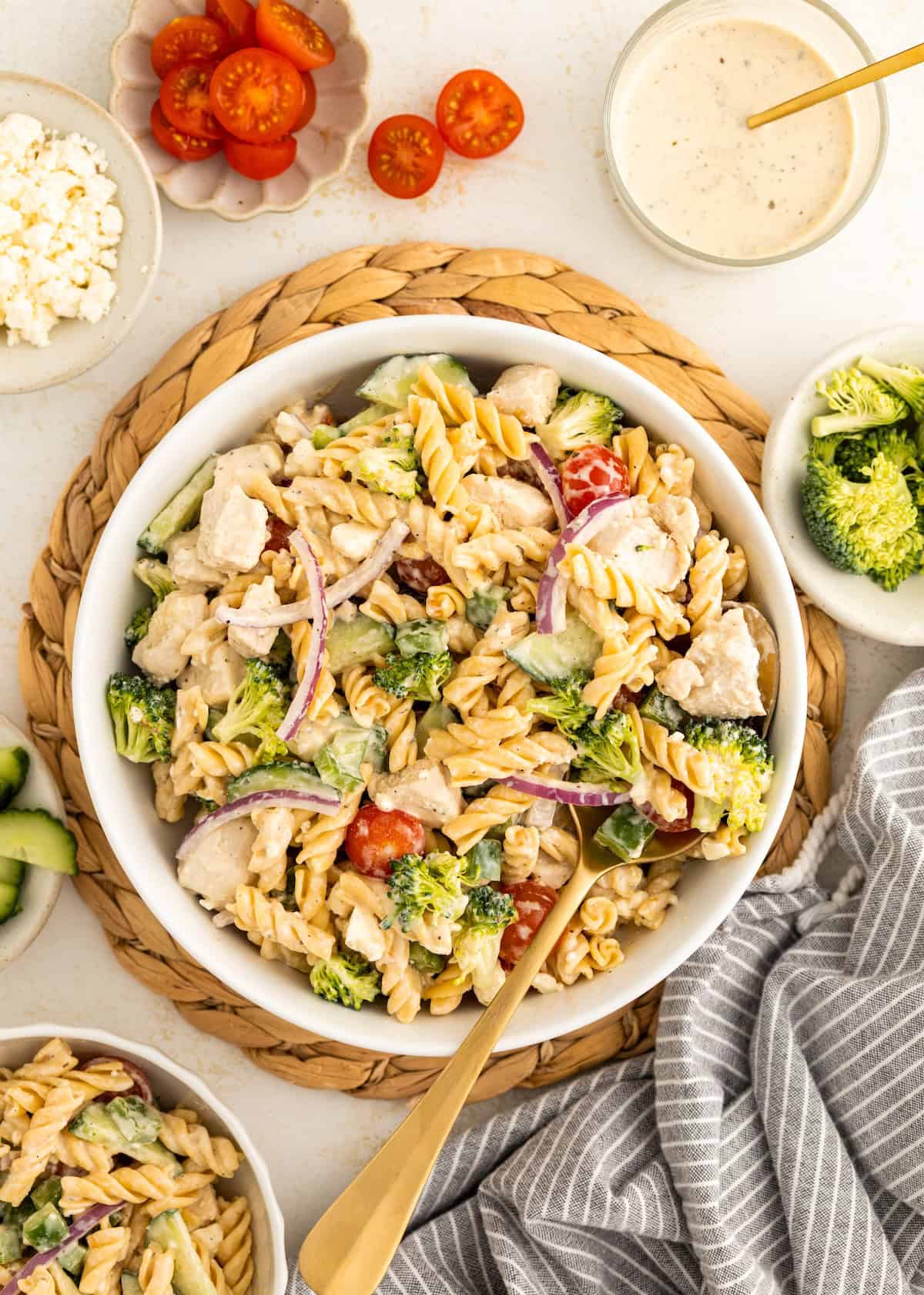 A bowl of protein pasta salad with chicken, broccoli, tomatoes, and red onion, plus a fork.