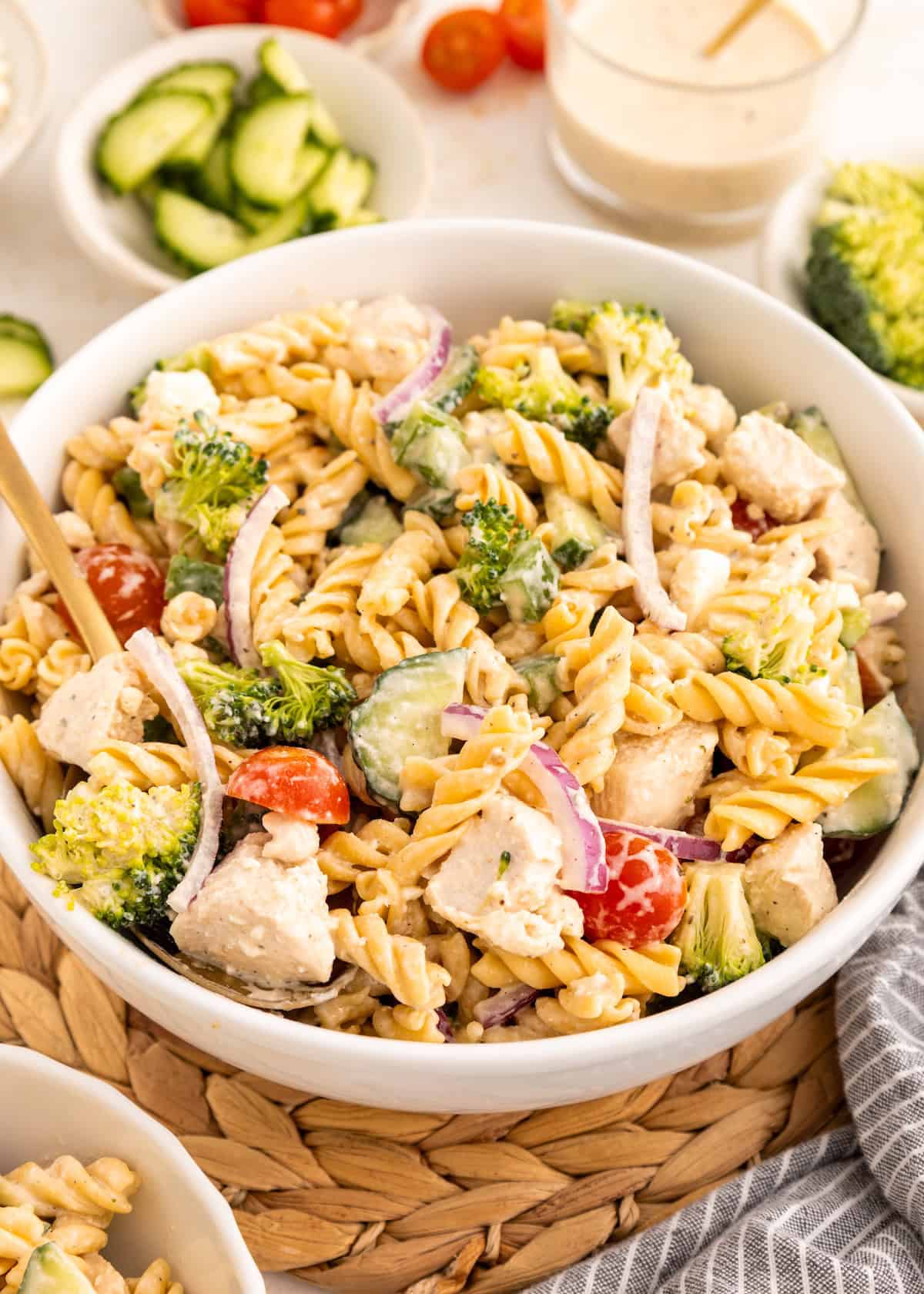 A bowl of protein pasta salad with chicken, broccoli, tomatoes, cucumbers, and red onion.