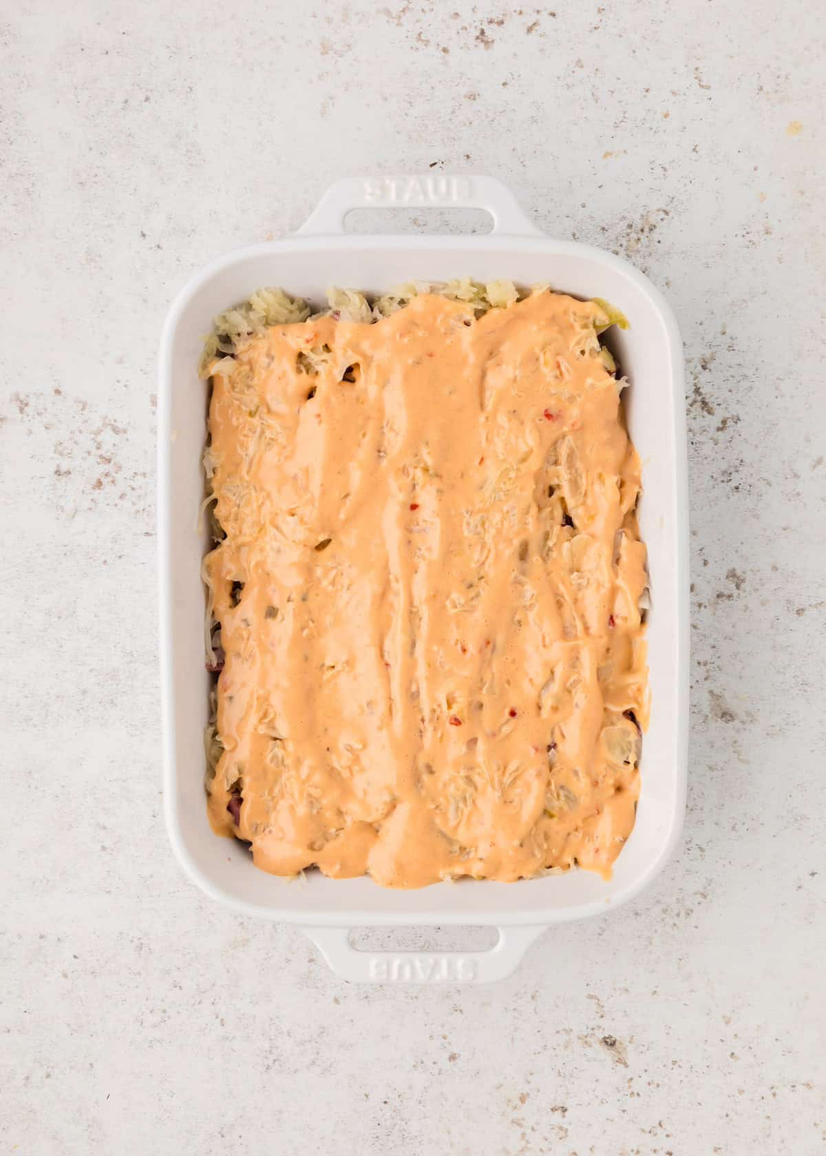 White baking dish with a creamy orange sauce spread over a layered casserole.