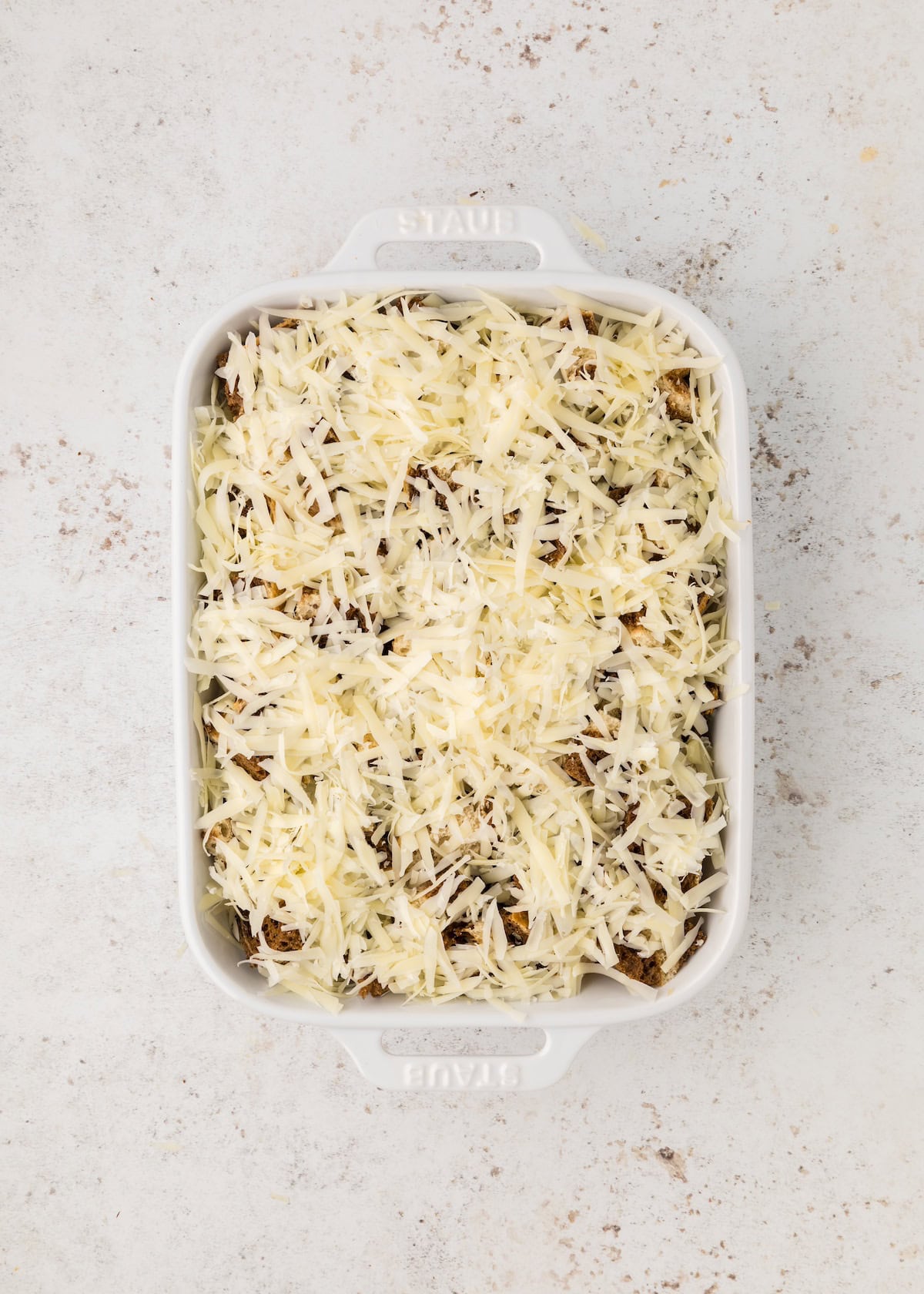 White baking dish filled with shredded cheese on top of a casserole, on a light background.