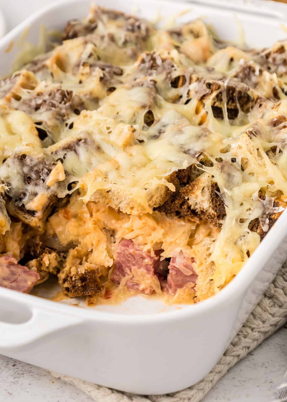 Casserole with melted cheese, bread pieces, and chunks of meat in a white baking dish.