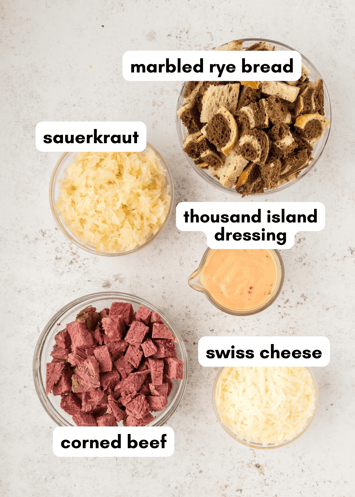 Five bowls with marbled rye bread, sauerkraut, swiss cheese, corned beef, and dressing.