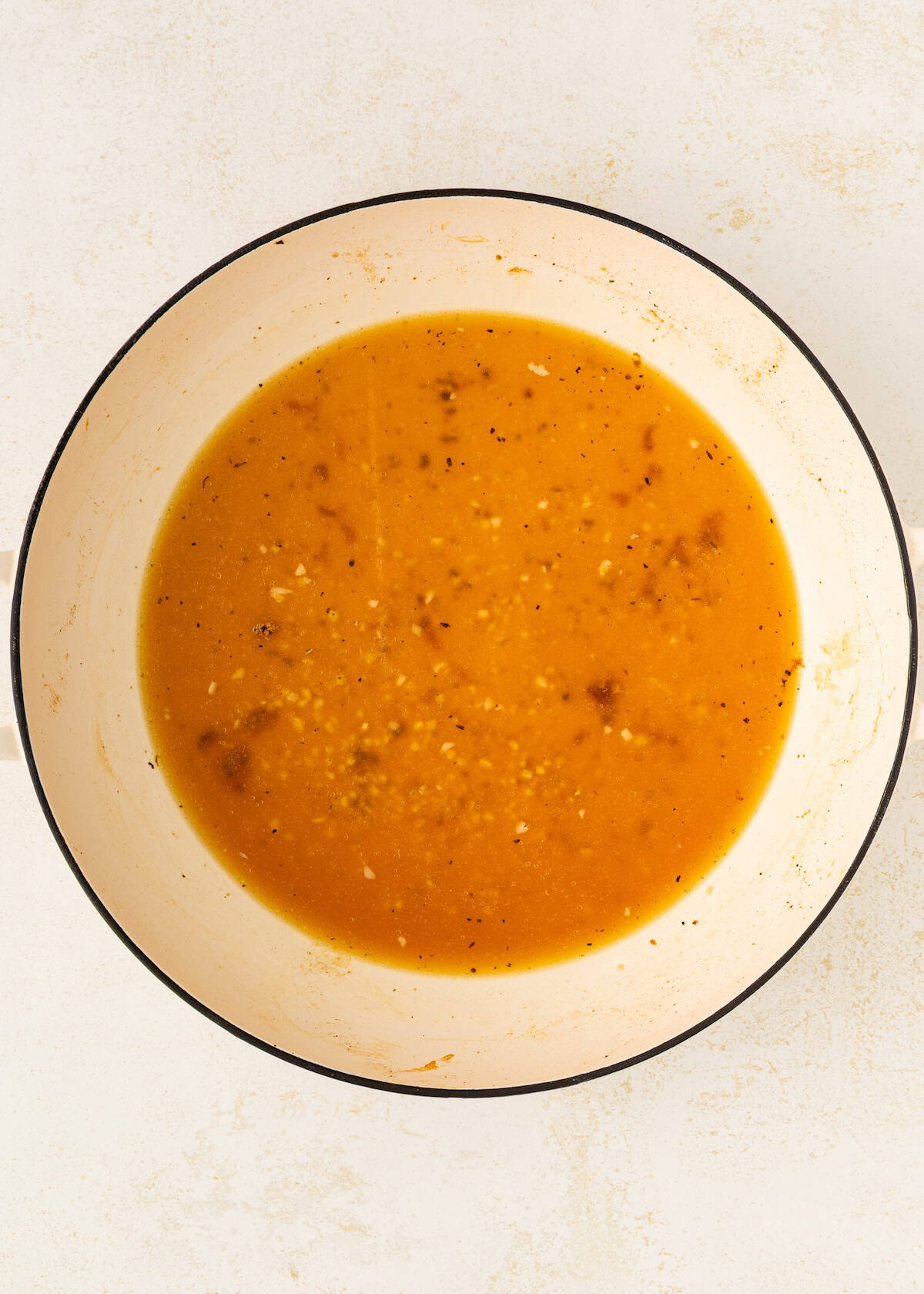 A pot of orange soup with seasonings on a light background.