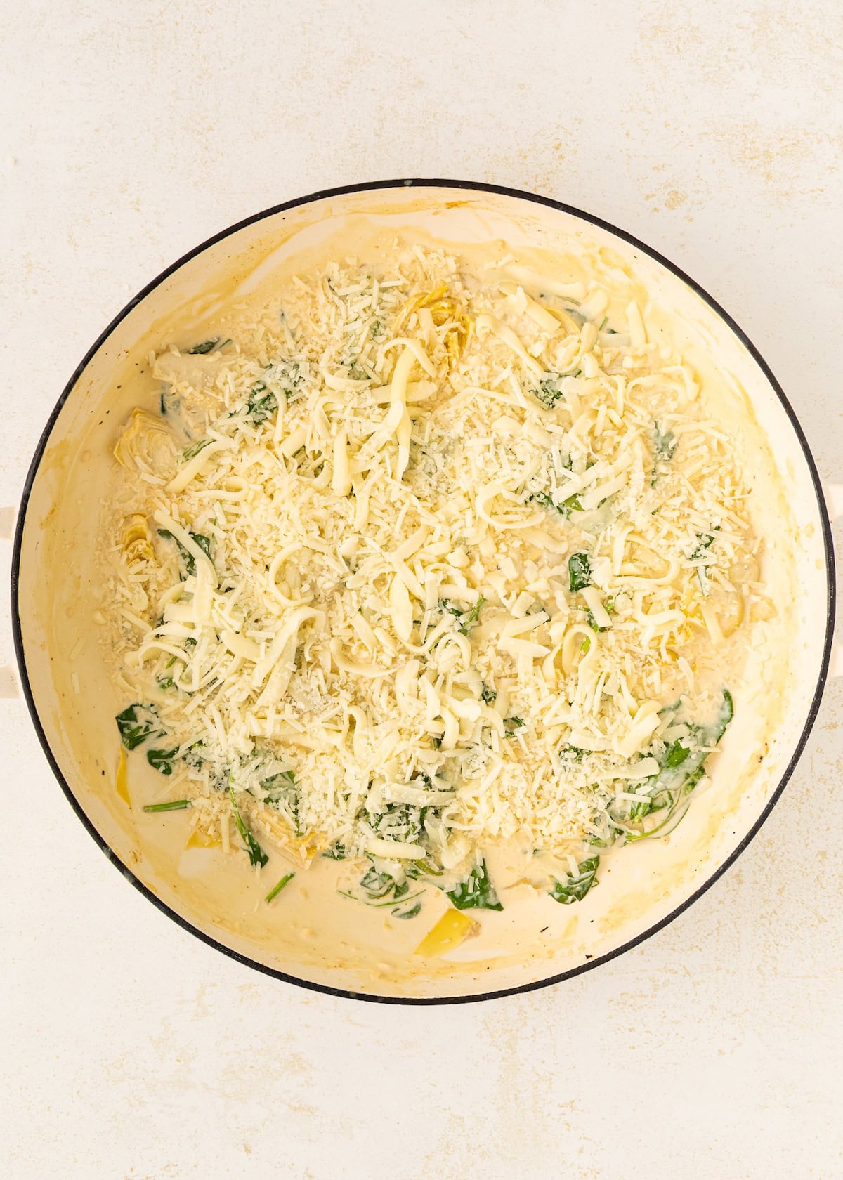 Creamy pasta with spinach and shredded cheese in a white pan on a light surface.