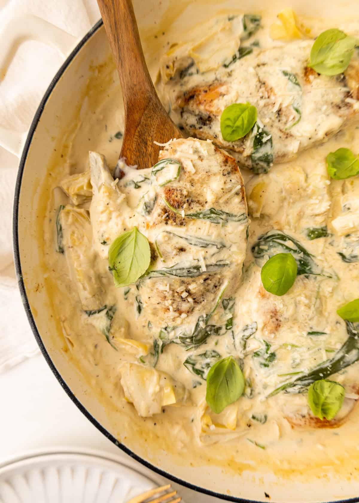 Creamy chicken with spinach and artichokes in a skillet, garnished with fresh basil leaves.