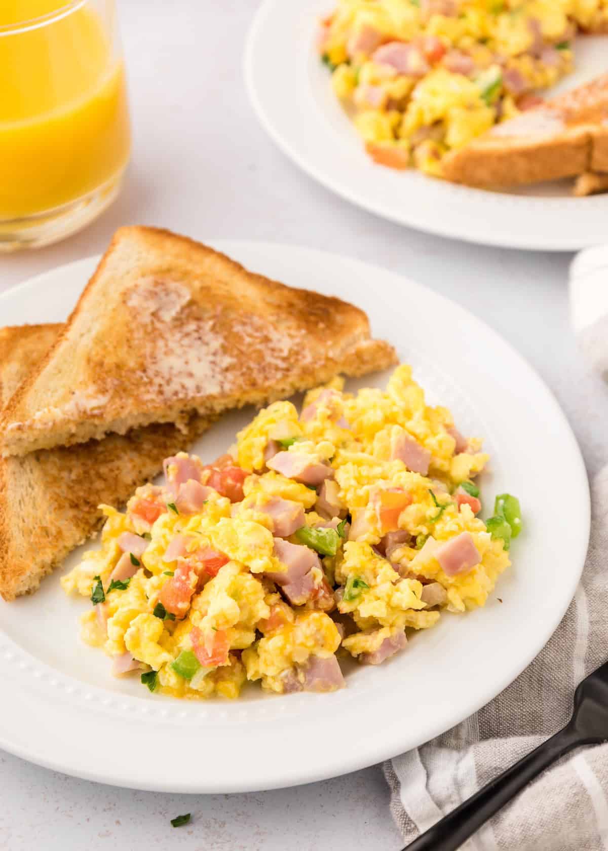 Scrambled eggs with ham and veggies, two slices of toast, and a glass of orange juice.