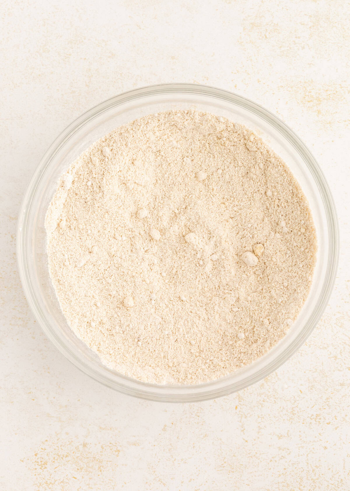 A glass bowl filled with finely ground flour on a light-colored surface.